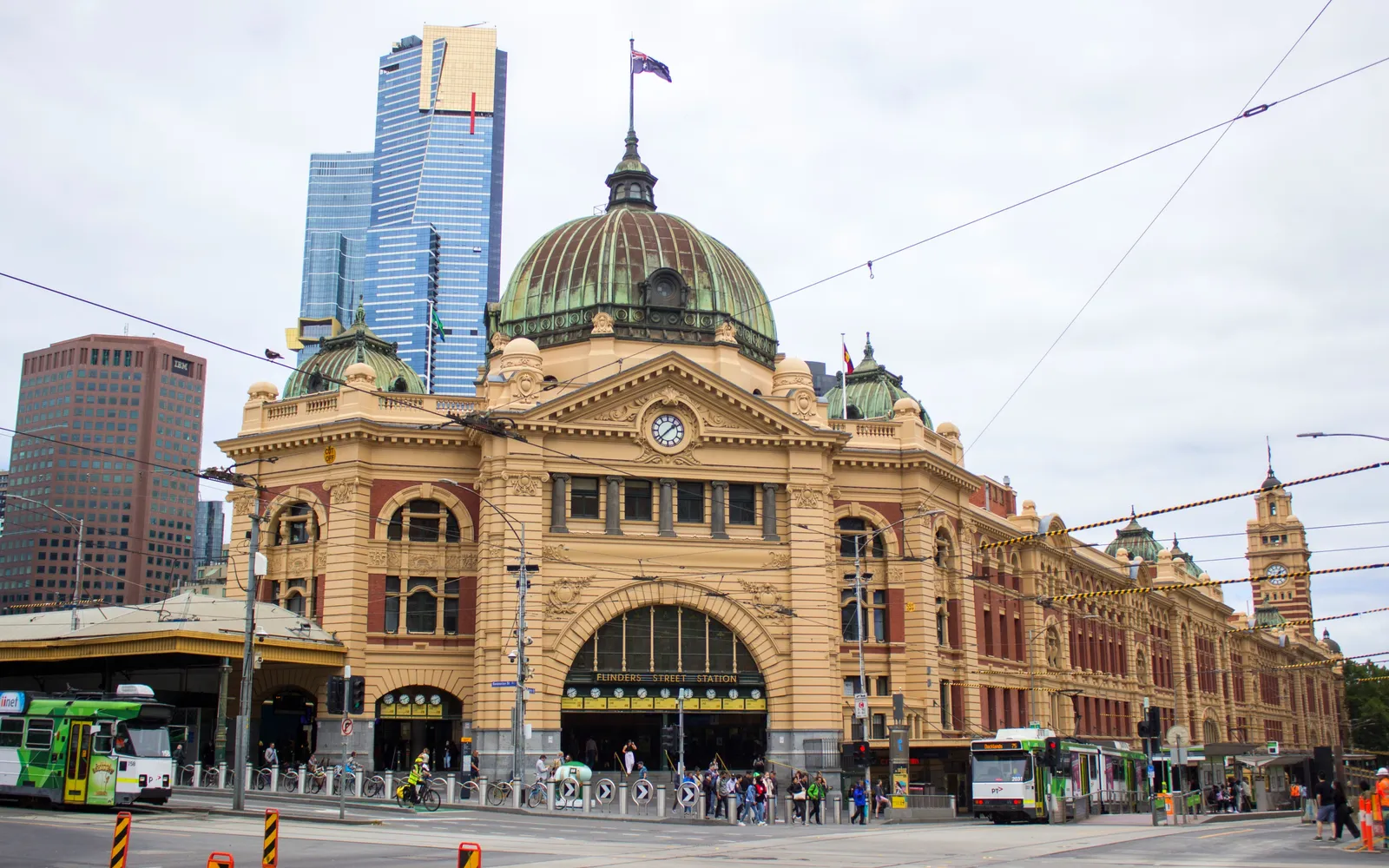 สถานีรถไฟ Flinders Street เมลเบิร์น หน้าอาคารสไตล์ Edwardian สีเหลืองทองโดมสีเขียวตั้งตระหง่าน นาฬิกาแถวบนหน้าจั่วแสดงเวลารถออก