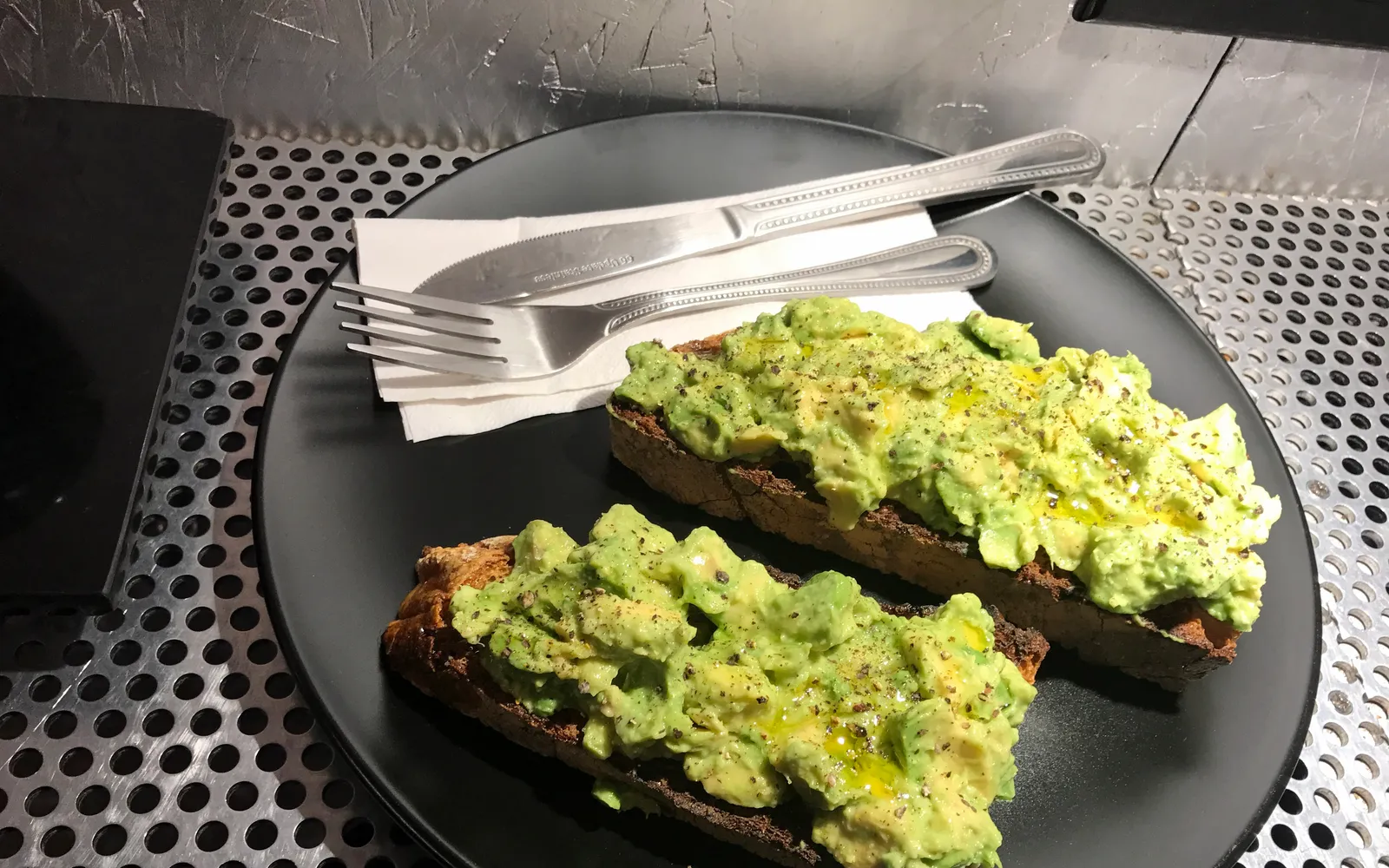 จาน smashed avocado บนขนมปังโซร์โดว์หนา โรยด้วยเฟต้าชีส ไข่ลวก ผักชีฝรั่ง และเม็ดทับทิมสีแดง