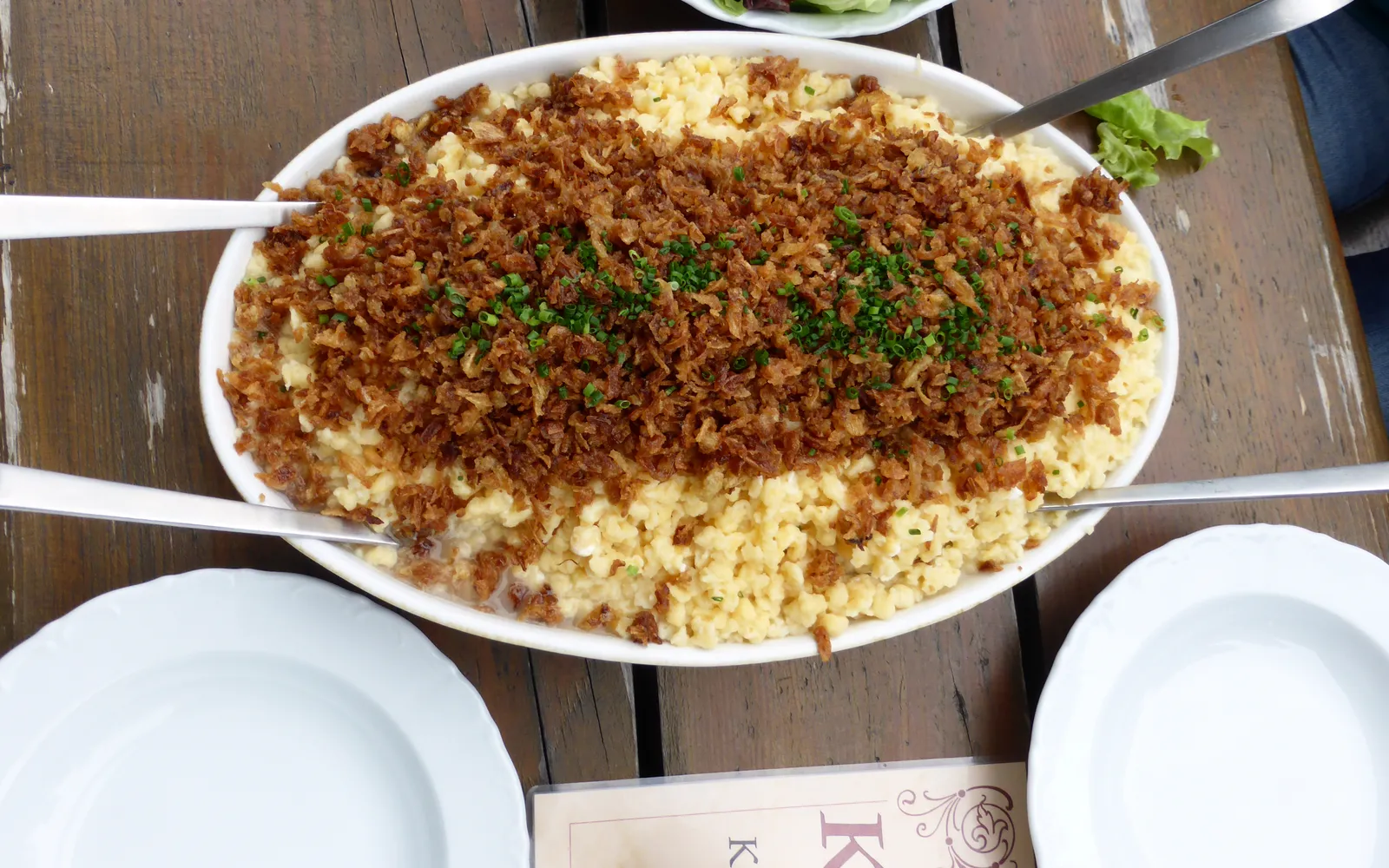 Käsespätzle ในจานดินเผาลึก เส้น Spätzle แป้งนุ่มคลุกชีสละลาย โรยหน้าด้วยหัวหอมทอดกรอบสีน้ำตาลทอง