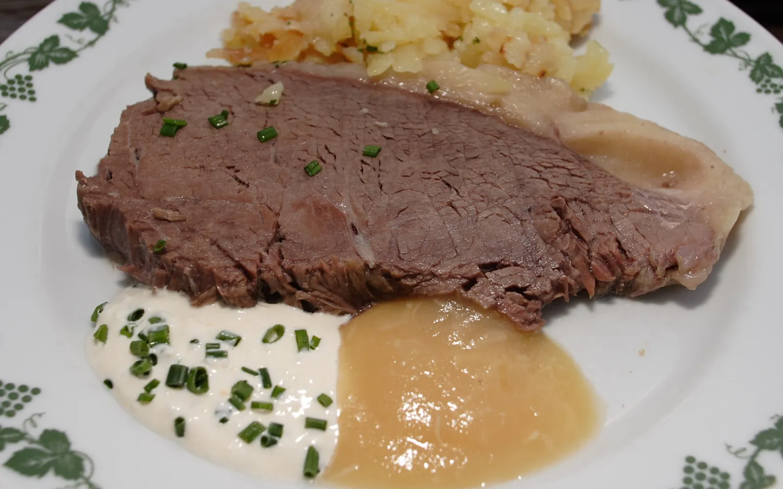Tafelspitz boiled beef in a clear golden broth in a deep bowl, served with root vegetables, horseradish and apple sauce, the meat tender and easy to cut