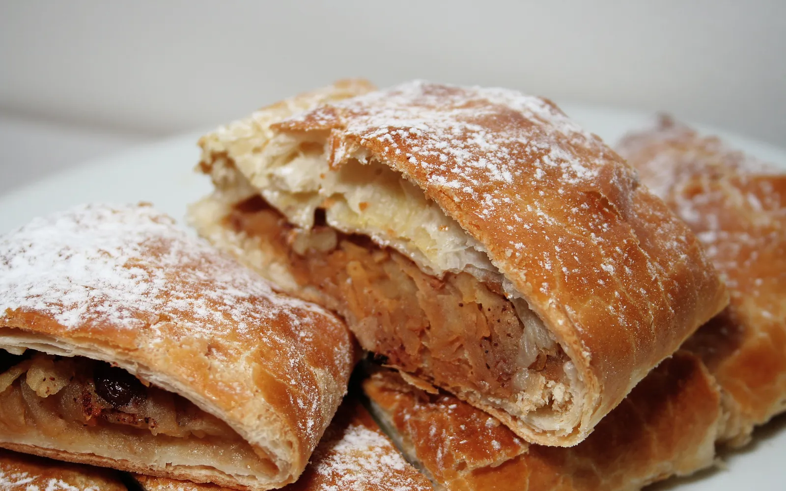 Apfelstrudel ชิ้นตัดร้อนๆ โรยน้ำตาลไอซิ่ง ไส้แอปเปิลอบกับอบเชยเห็นผ่านแป้งบางกรอบ เสิร์ฟพร้อมวิปครีมข้างๆ