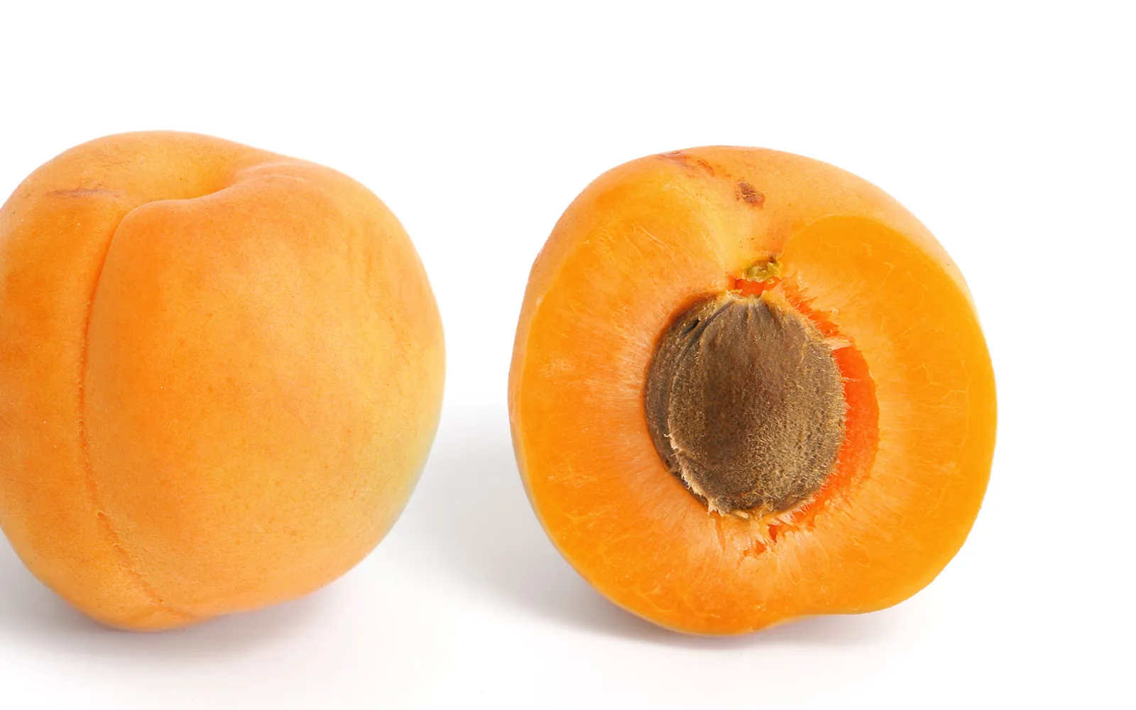 A jar of deep-orange Wachau apricot jam on a wooden table, with fresh apricots and a thick-crusted loaf of Bauernbrot