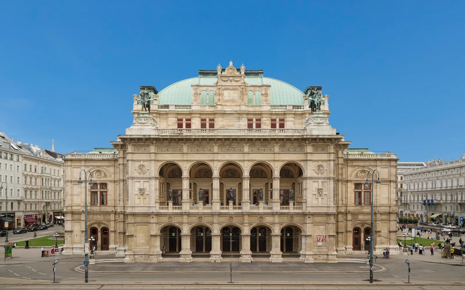 The neo-Renaissance facade of the Vienna State Opera, marble arches and gilded statues glowing at night as elegantly dressed operagoers climb the stairs