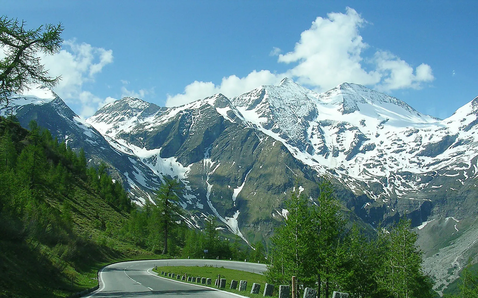 ถนนคดเคี้ยวบนเทือกเขา Grossglockner High Alpine Road ผ่านเนินหิมะขาวและยอดเขาแหลมคมสีเทา