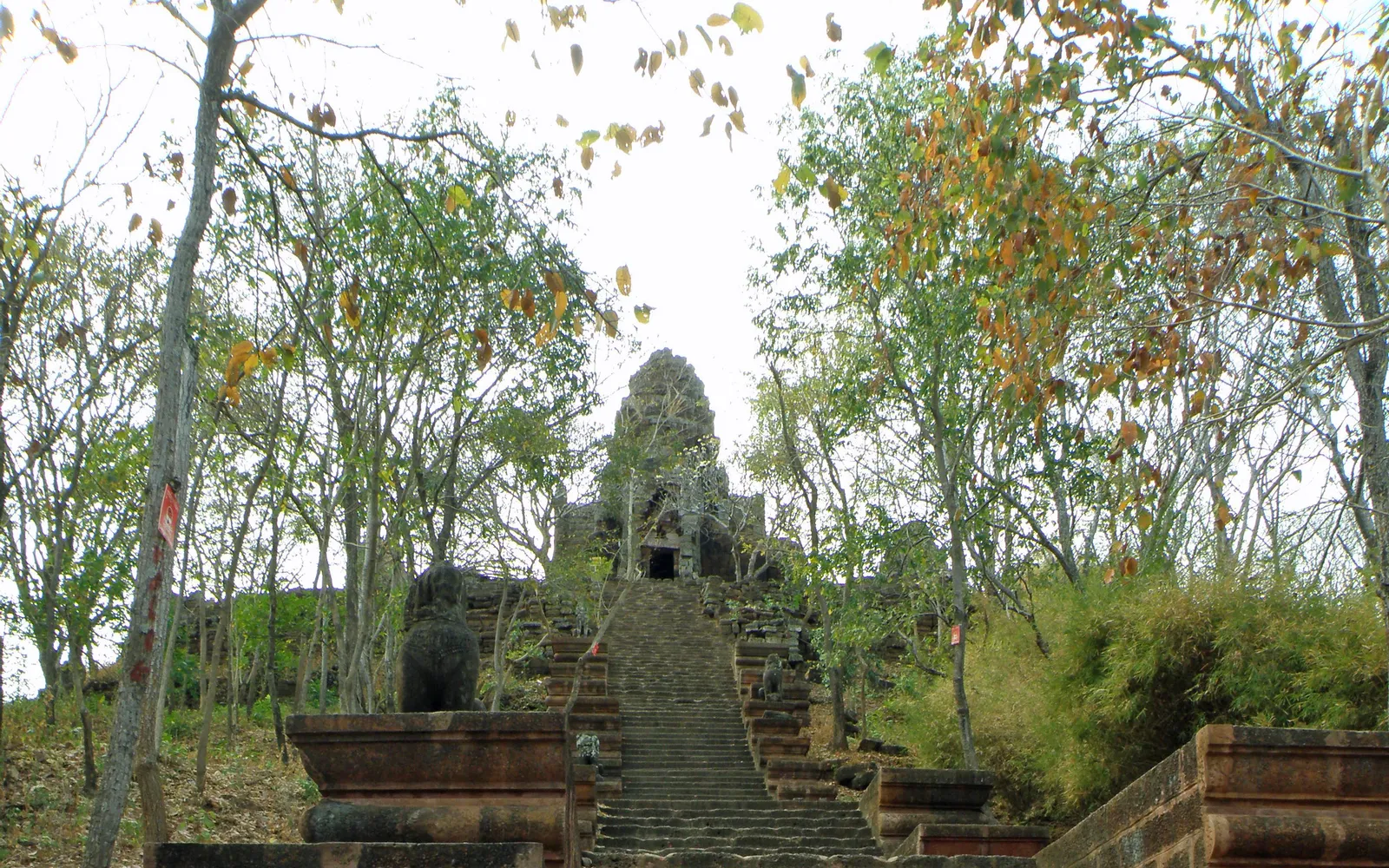 ปรางค์ห้ายอดของวัดบานนบนยอดเขาพระตะบอง ยอดแหลมหินทรายแดงตัดท้องฟ้าสีฟ้า รายล้อมด้วยต้นไม้เขียว