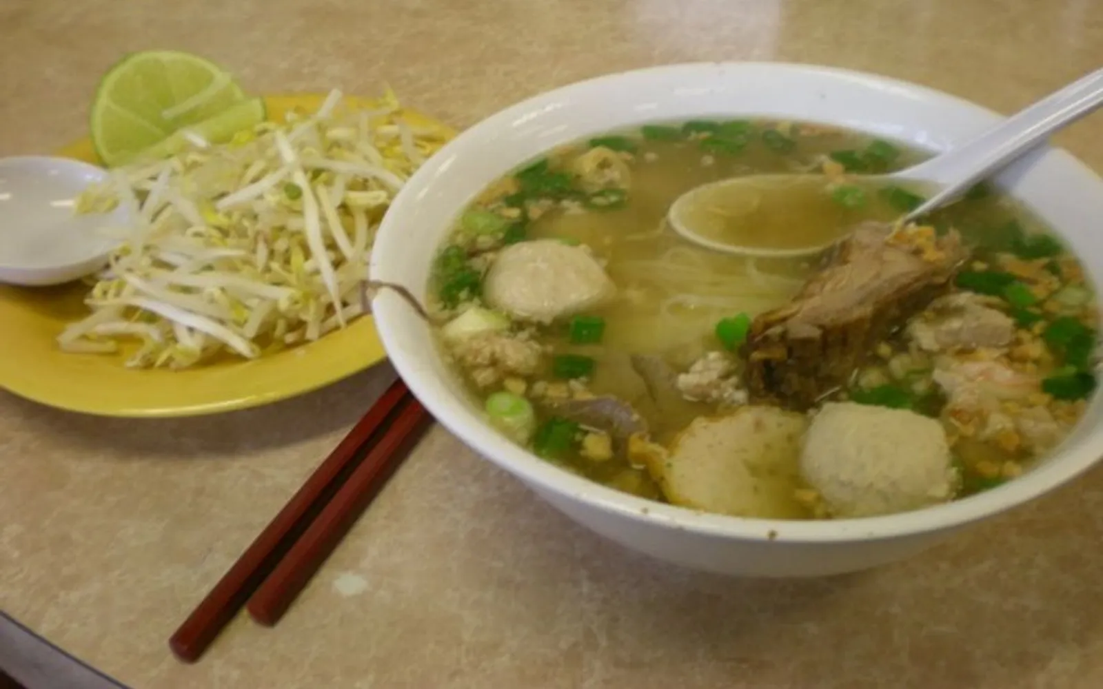 ก๋วยเตี๋ยวกุ้ยเตียวชามใหญ่ น้ำซุปใสสีทอง เส้นข้าวขาว หมูสับ ลูกชิ้น ต้นหอม และผักชีลาว