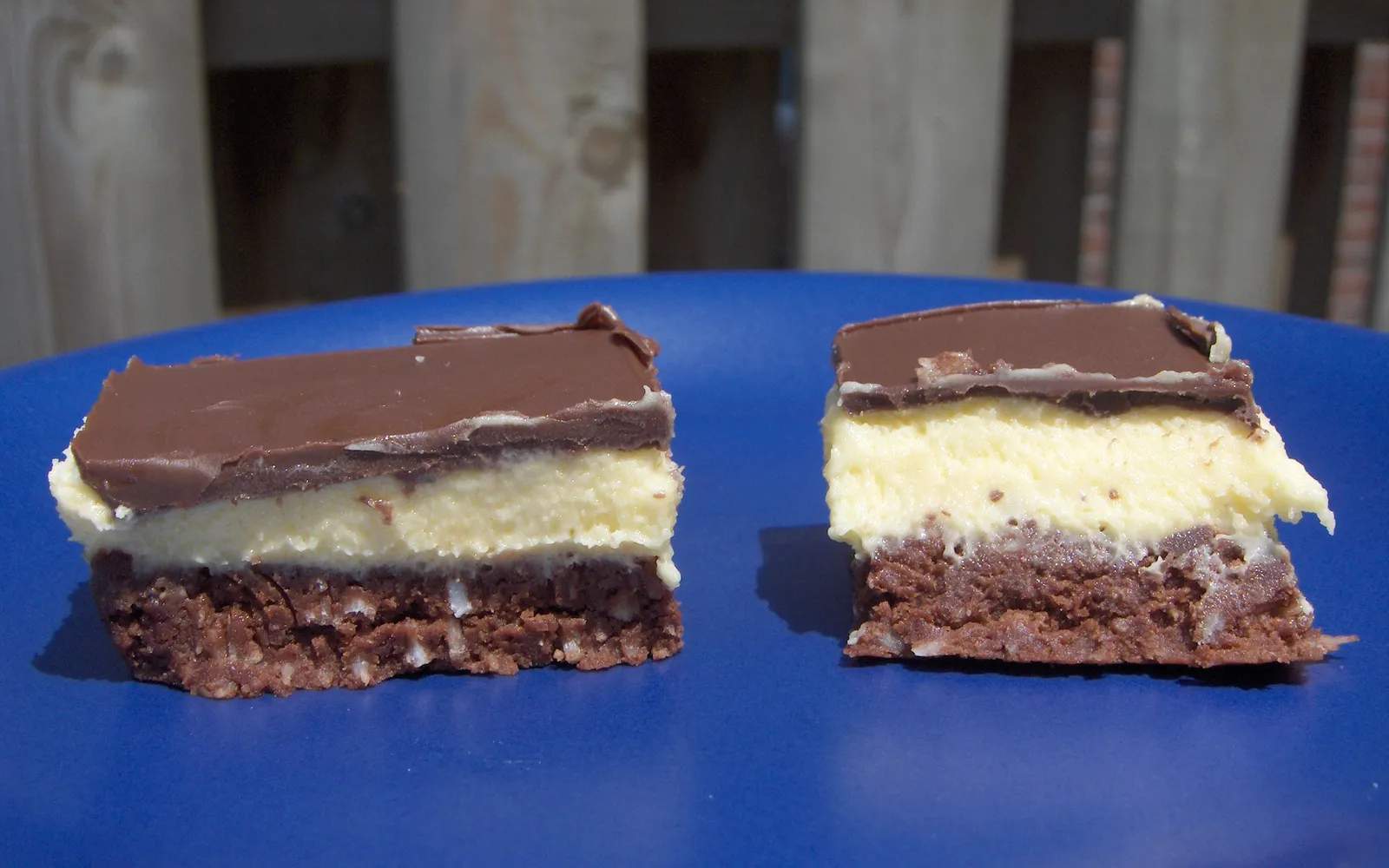Nanaimo bar ขนมแคนาเดียนสามชั้น ฐานช็อกโกแลตโกโก้ กลางครีมเนยวานิลลา บนช็อกโกแลตเคลือบเงา หั่นเป็นชิ้นสี่เหลี่ยม