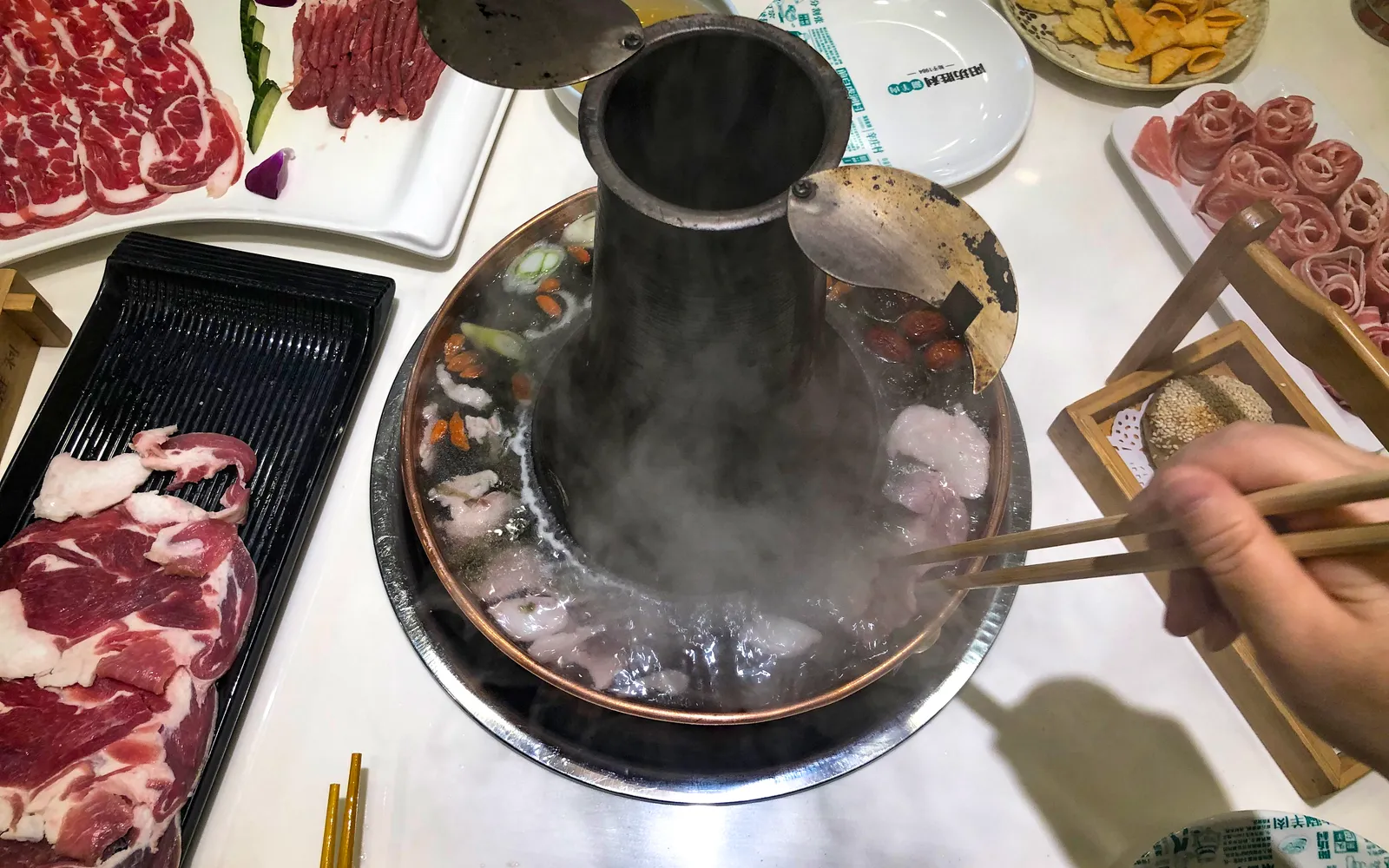 หม้อทองแดงทรงโดนัทกลางโต๊ะพร้อมเนื้อแกะแล่บางและน้ำซุปใส