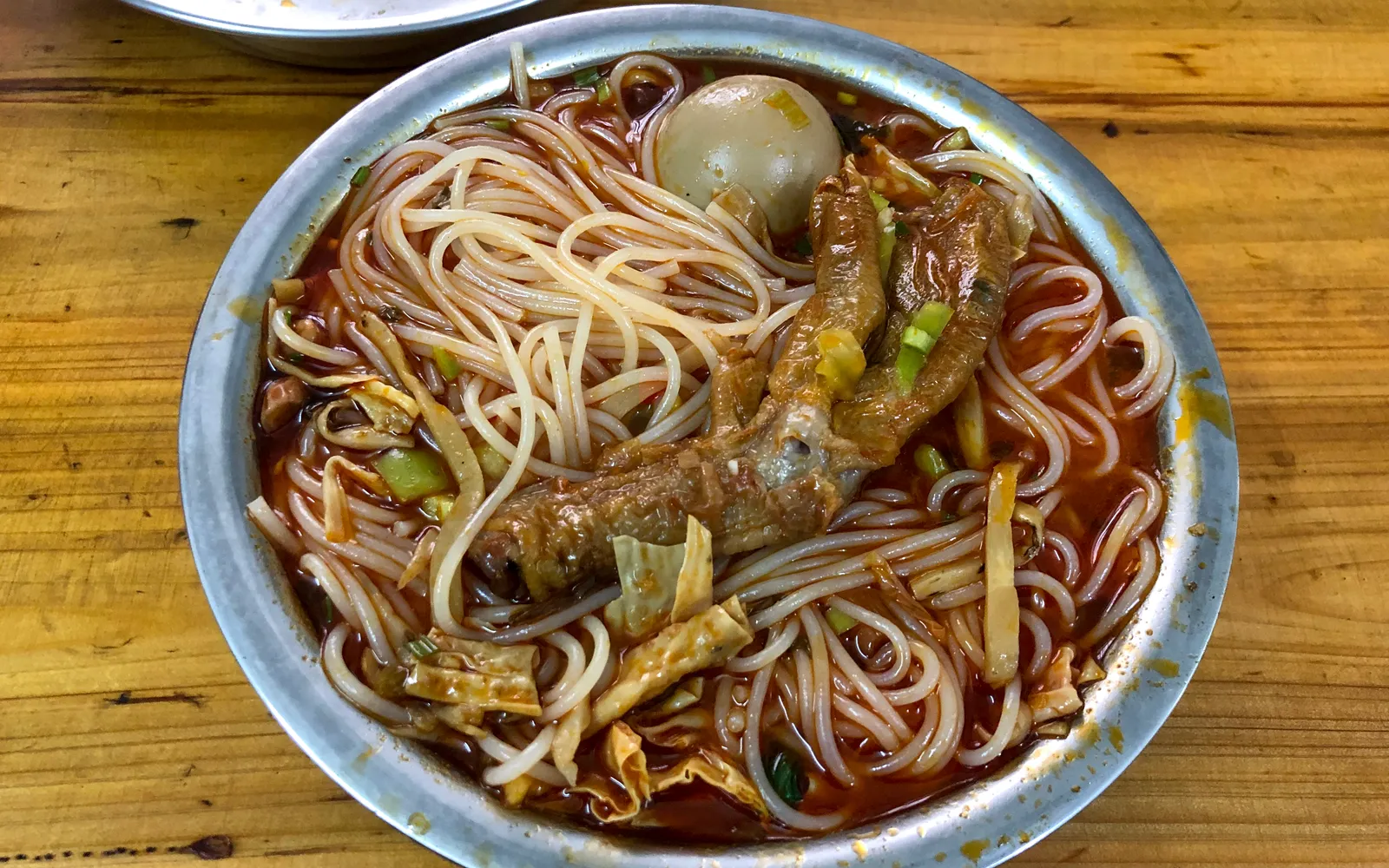 หมี่หอยทากสไตล์กุ้ยหลิน ชามลึกใส่เส้นข้าว น้ำซุปหอยทากสีส้มข้น ท็อปด้วยผักกาดดอง ถั่วฝักยาว เต้าหู้ทอด และพริกแดง