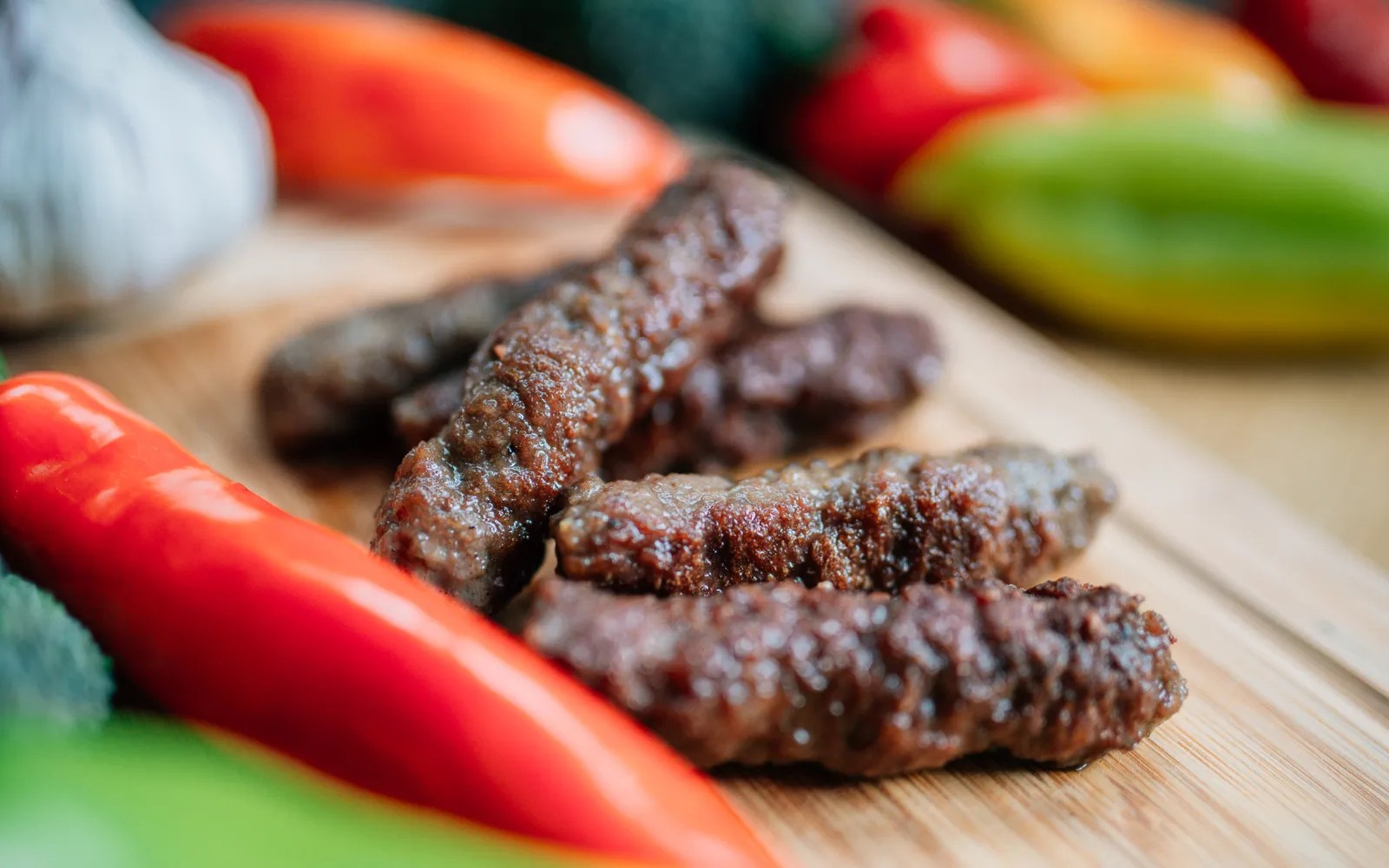 Ćevapi เนื้อบดย่างรูปทรงกระบอกเรียงในขนมปัง lepinja เสิร์ฟพร้อม ajvar พริกแดงและหัวหอมสับ