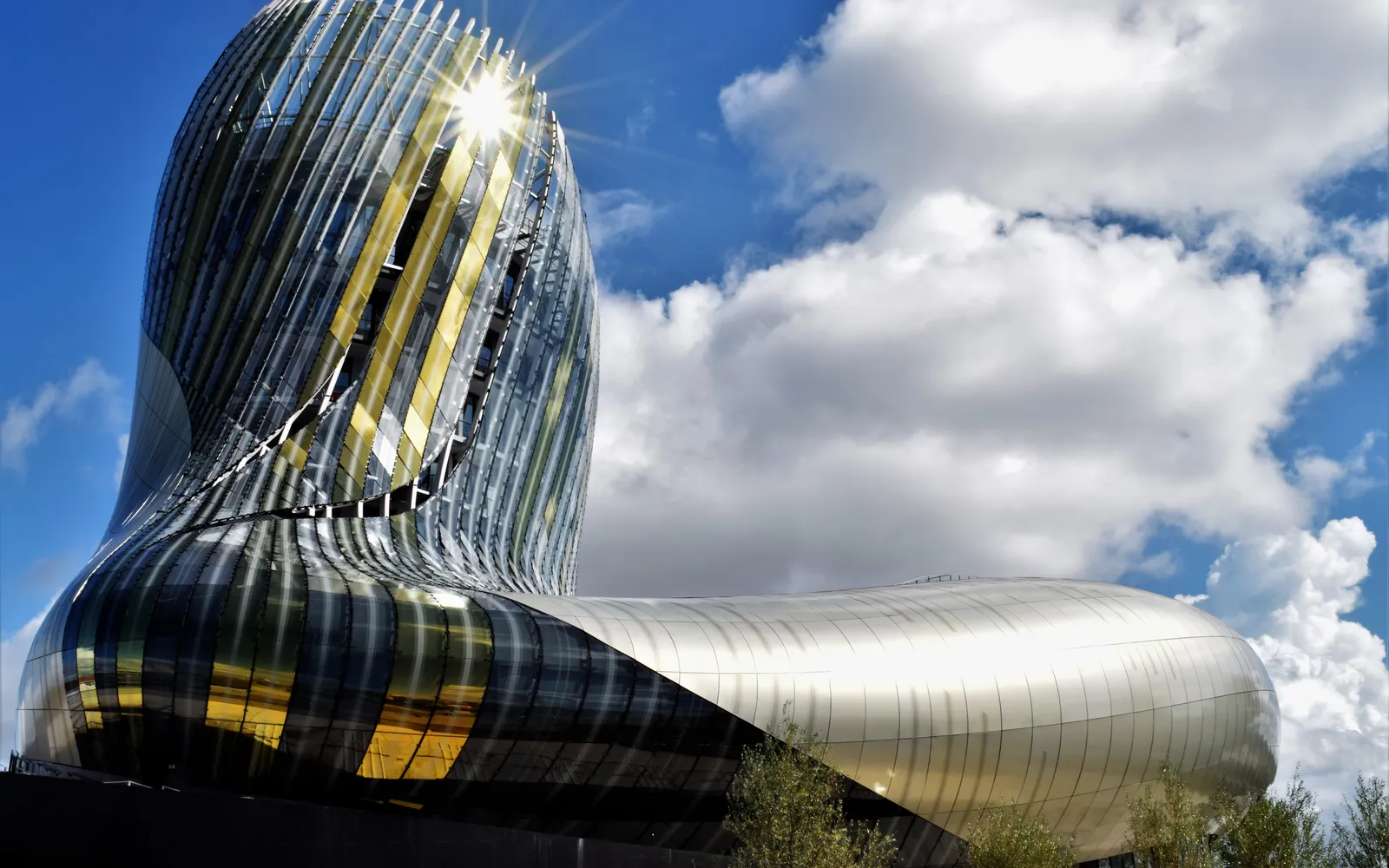 อาคาร Cité du Vin บอร์โด รูปทรงโค้งเกลียวสีทองบิดเหมือนไวน์ในแก้ว ตั้งโดดเด่นริมแม่น้ำการอนใต้ท้องฟ้าสีฟ้า