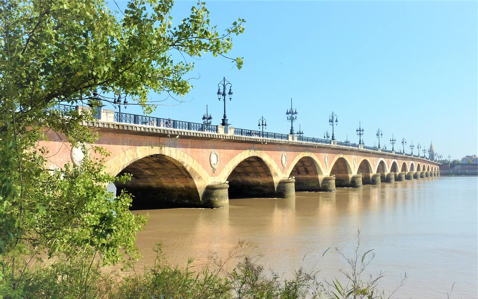 สะพาน Pont de Pierre บอร์โด โค้งหินทั้ง 17 โค้งสะท้อนบนแม่น้ำการอนยามเย็น ฝั่งซ้ายแลเห็นอาคารประวัติศาสตร์แถวริมน้ำสีครีม