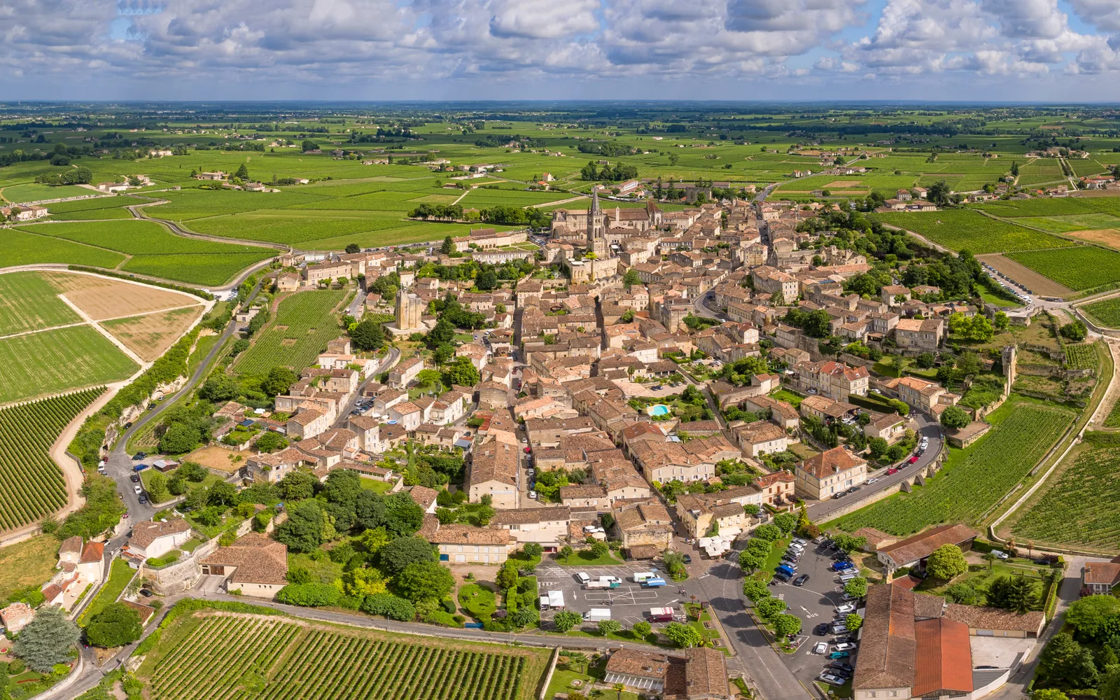 หมู่บ้าน Saint-Émilion บนเนินเขา หลังคากระเบื้องสีส้มแดงของบ้านหินยุคกลางเรียงซ้อนกันท่ามกลางไร่องุ่นสีเขียวที่ทอดยาวไปถึงขอบฟ้า