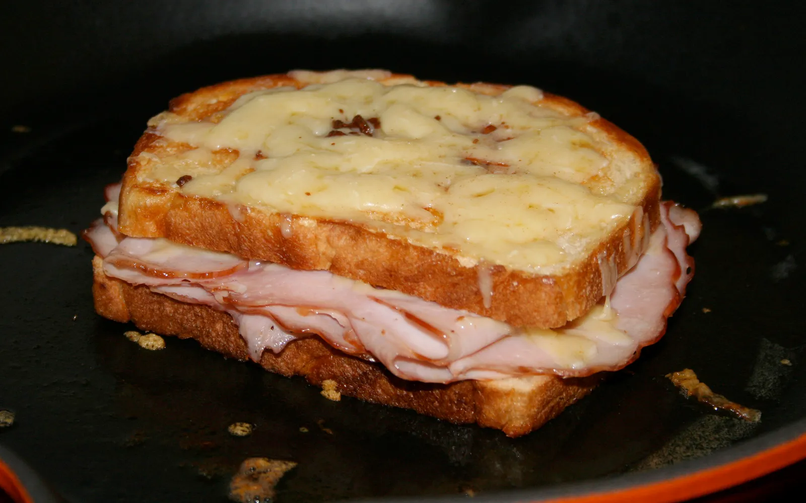 ครอกมัวซิเออบนจานขาว ขนมปังอบทองพร้อมเนยแข็ง Gruyere ละลายไหลออกสีเหลืองทอง ข้างๆ มีสลัดใบเล็กๆ