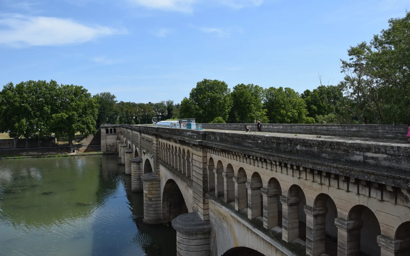 คลอง Canal du Midi ตูลูส ต้นเพลนสูงใหญ่ทอดร่มเงาสองข้างคลอง เรือบ้านสีสันจอดเรียงตามฝั่ง น้ำสะท้อนใบไม้สีเขียว