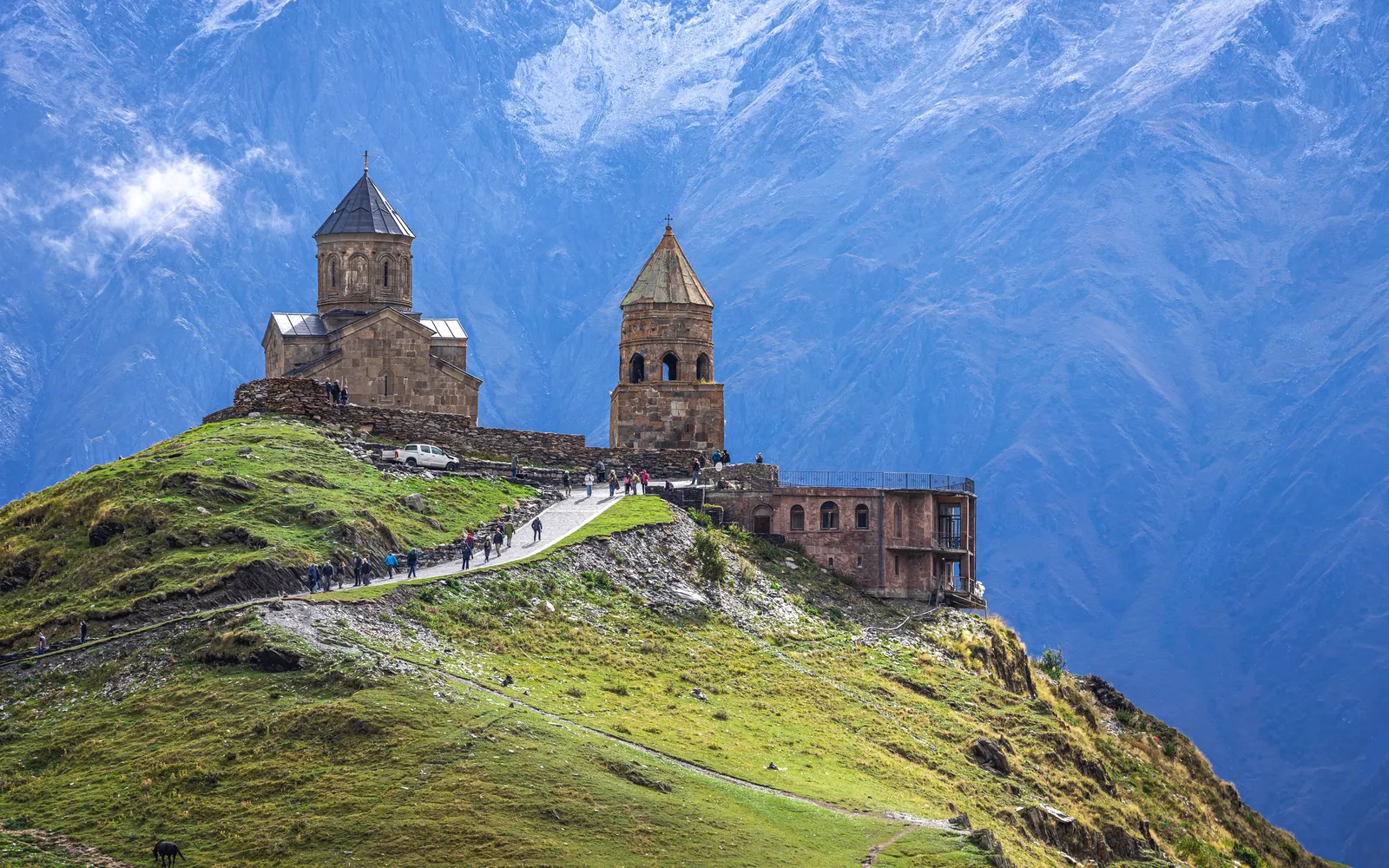 วัดเกิร์เกติ ทรินิตีบนเนินเขาสูงเหนือเมืองกาซเบกี ยอดเขา Kazbek ที่ปกคลุมด้วยหิมะตั้งตระหง่านอยู่เบื้องหลัง