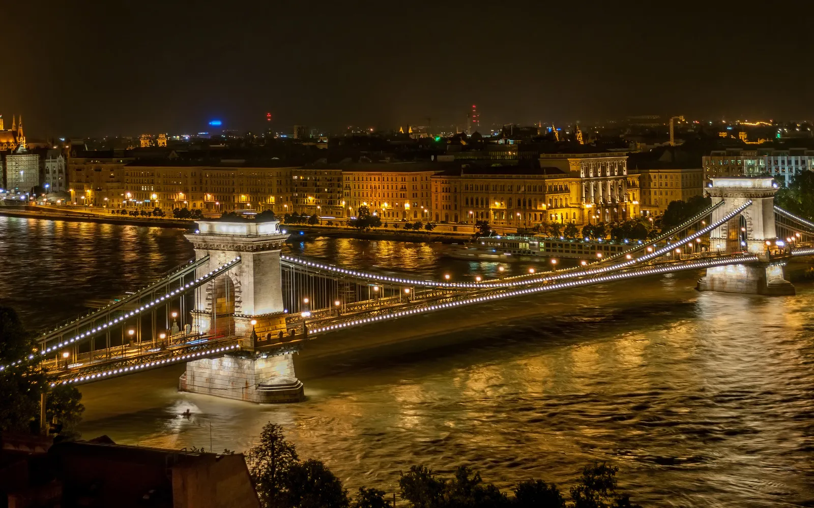 สะพาน Chain Bridge บูดาเปสต์ยามค่ำ ไฟส่องสว่างห่วงโซ่เหล็กสีทองทอดยาวข้ามแม่น้ำดานูบ ปลายสะพานทั้งสองฝั่งมีสิงโตหินเฝ้าอยู่