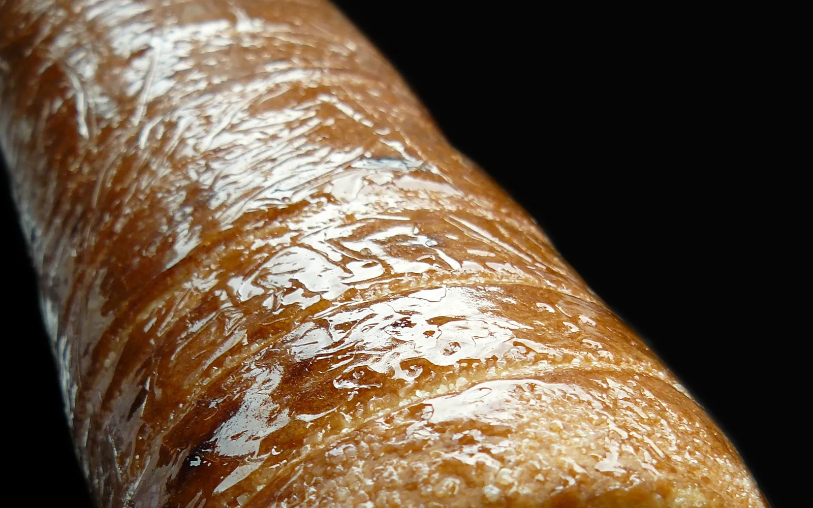 Kürtőskalács ขนมปังม้วนฮังการีทรงกระบอก เปลือกนอกสีทองกรอบเคลือบน้ำตาลและอบเชย บนแท่งไม้ที่กำลังหมุนเหนือถ่านร้อน