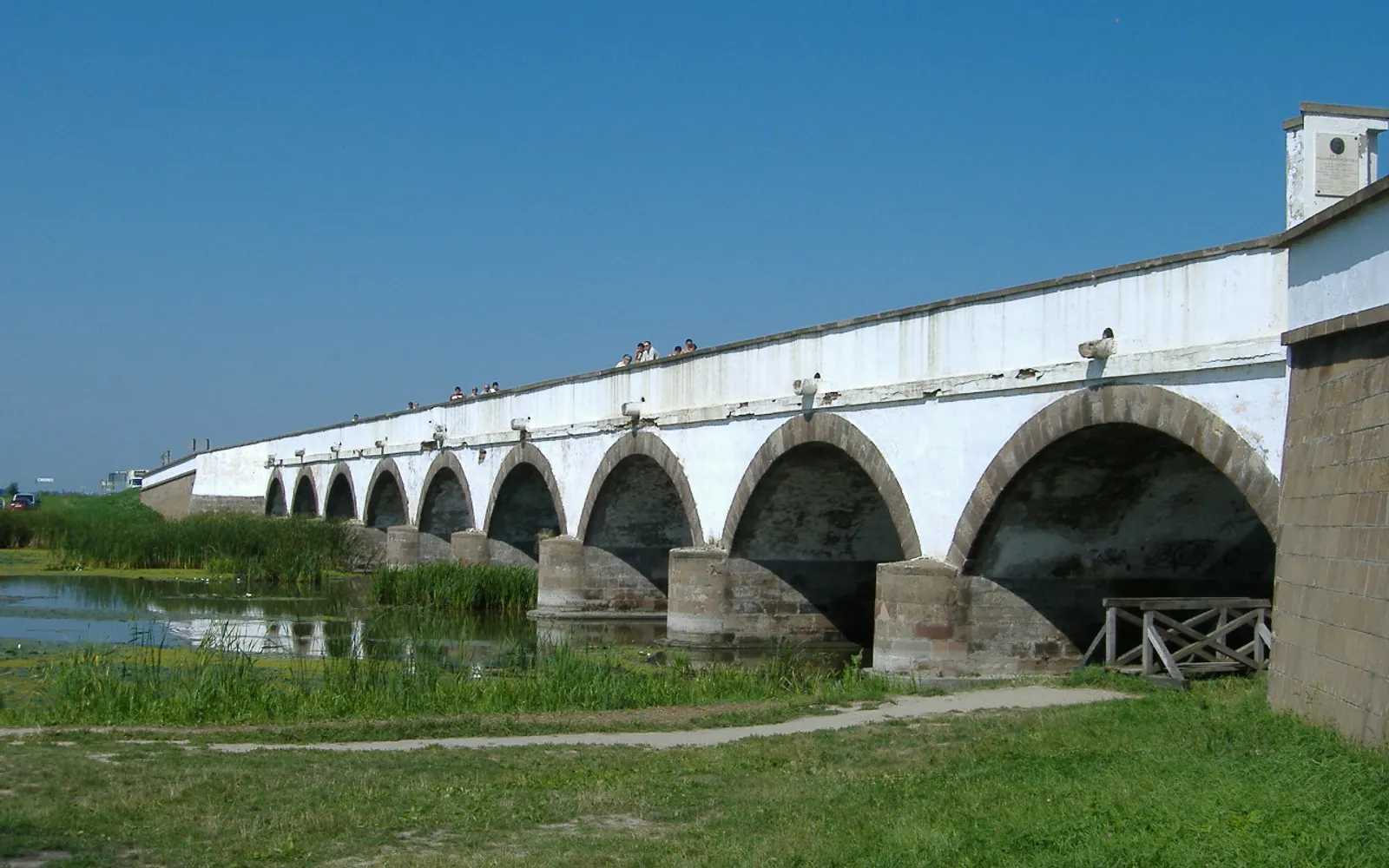 สะพานหินเก้าโค้ง Nine-Arch Bridge แห่ง Hortobágy ทอดข้ามแม่น้ำ Hortobágy สะท้อนภาพในน้ำเรียบ ทุ่งหญ้า Puszta โล่งตัดกับท้องฟ้า