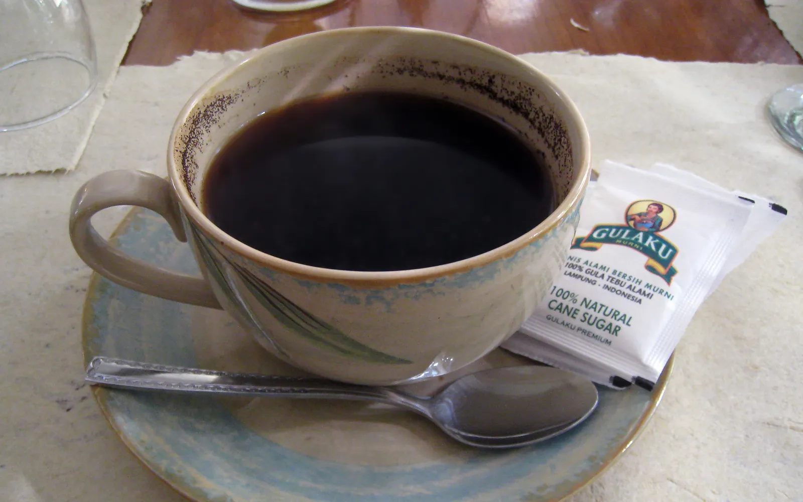 แก้วกาแฟฟลอเรสโรบัสตาสีน้ำตาลเข้ม เสิร์ฟในแก้วใสพร้อมน้ำเปล่าในคาเฟ่ท้องถิ่นบรรยากาศเรียบง่าย