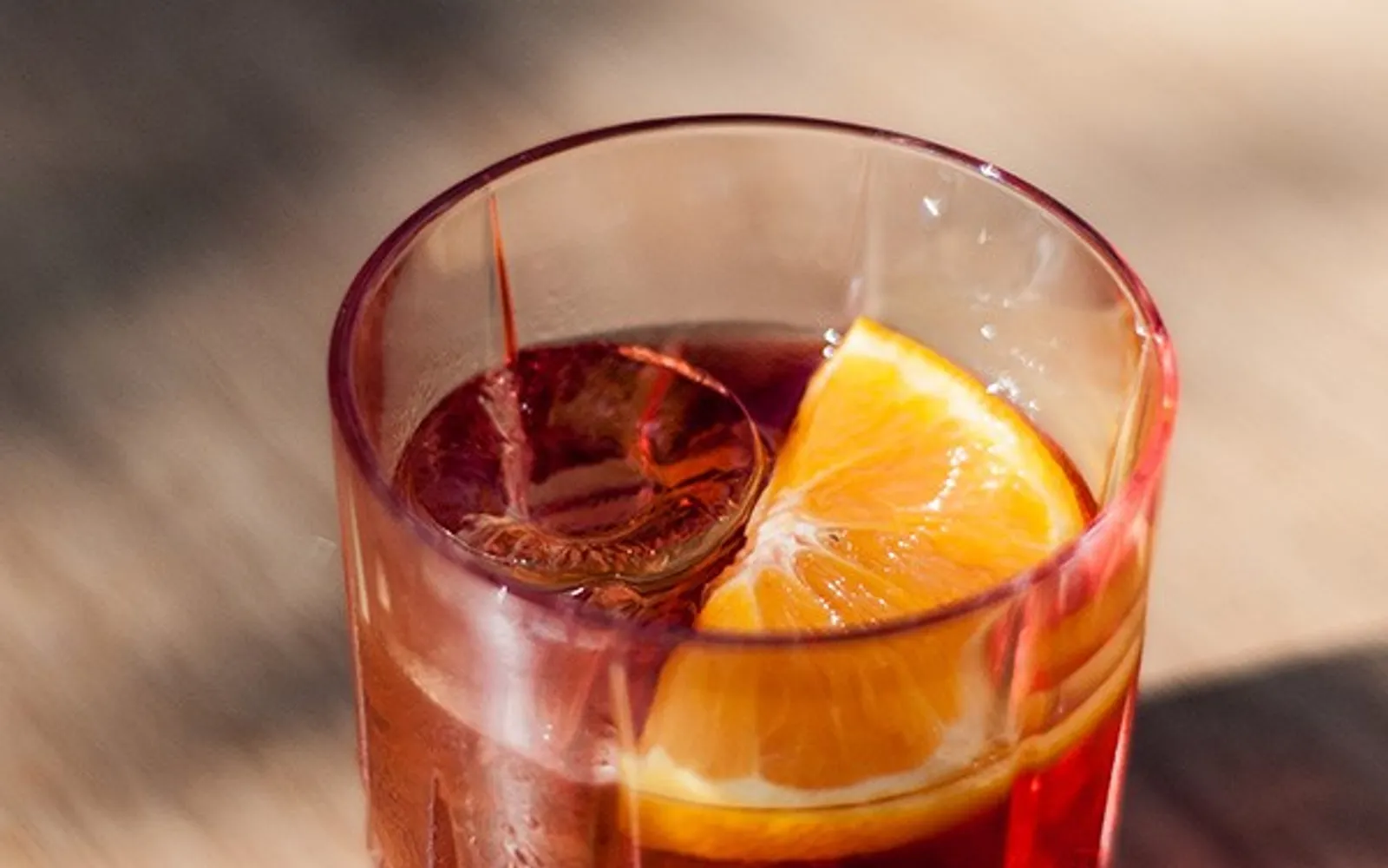 แก้ว Aperol Spritz สีส้มสดใสบนบาร์ไม้ ด้านหลังมีจานของว่างเรียงราย ไฟสีอุ่นและบรรยากาศยามเย็นของบาร์มิลาน