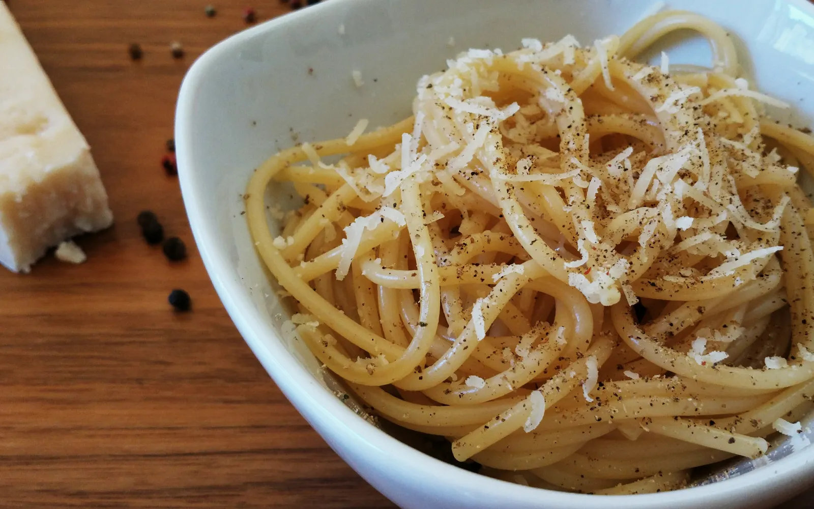 Cacio e pepe in a deep white bowl — spaghetti napped in a pale-yellow creamy Pecorino Romano sauce, with coarsely ground black pepper scattered evenly on top