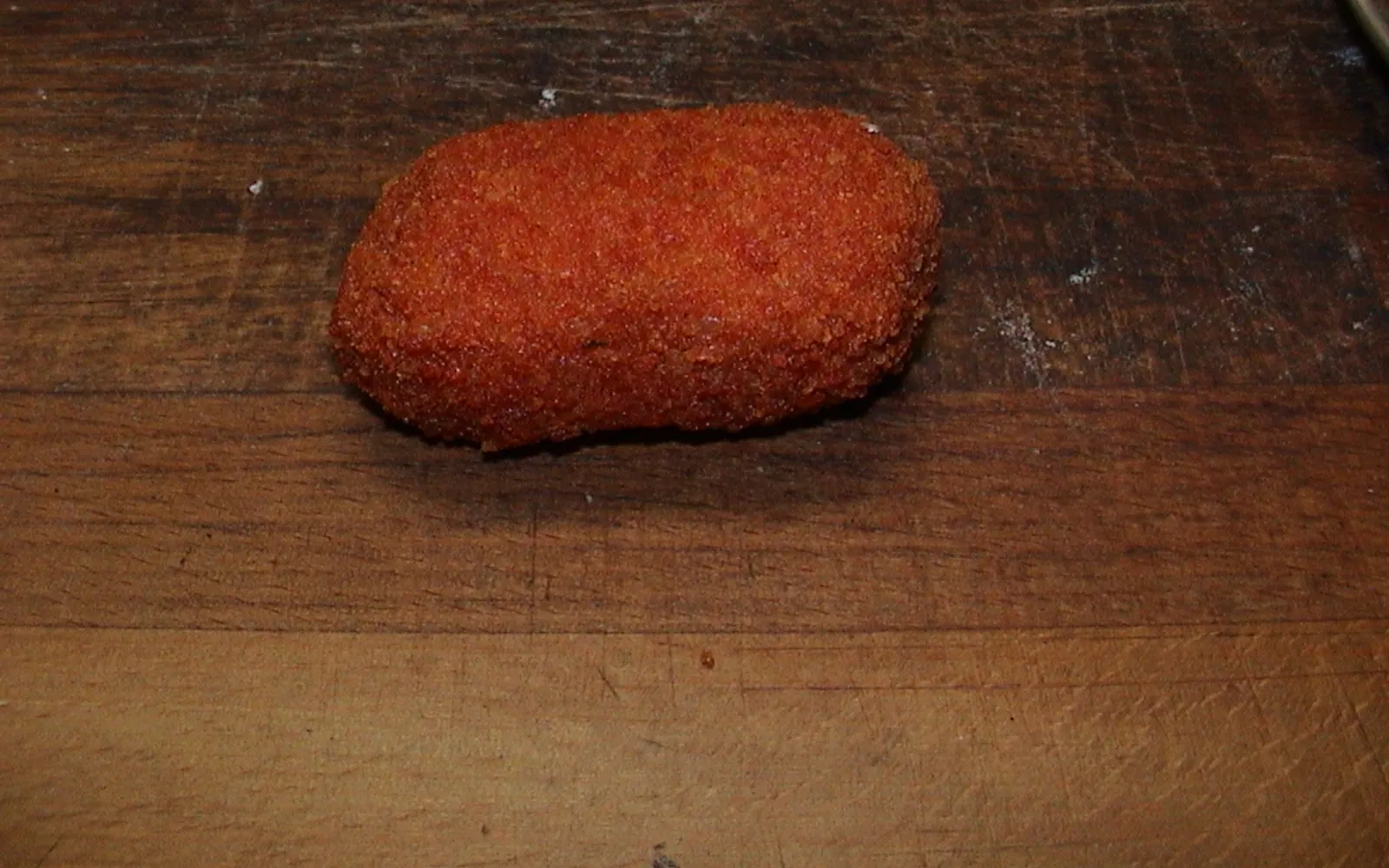 Two supplì on a sheet of greaseproof paper — golden-brown crisp exterior; when broken in half, revealing red tomato-sauce risotto and a long stretching thread of white mozzarella
