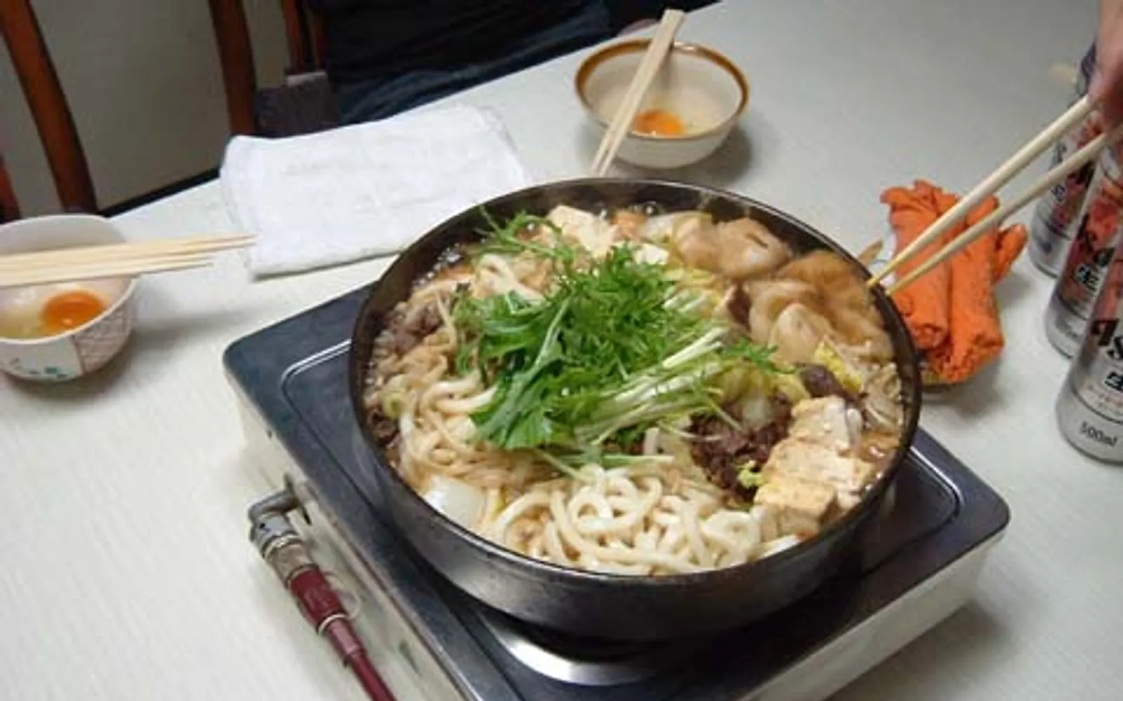 หม้อมิซุทากิน้ำซุปใสพร้อมไก่และผักสดวางอยู่บนเตาถ่านกลางโต๊ะ