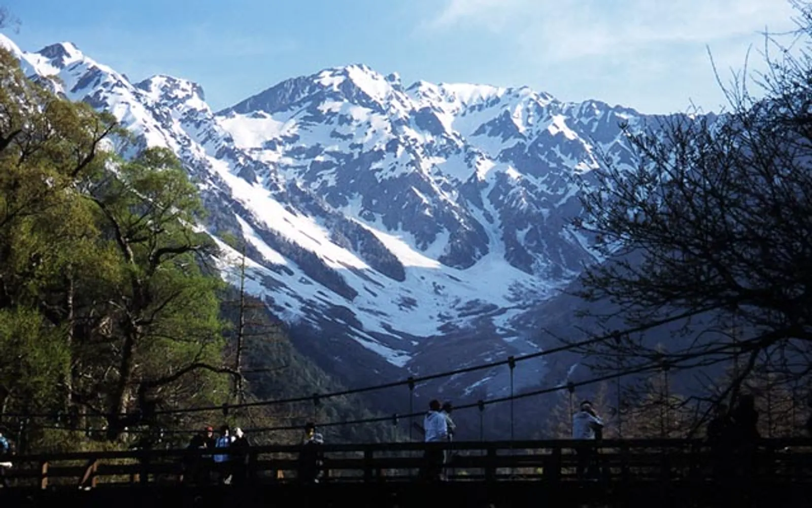 สะพาน Kappa-bashi สีน้ำเงินพาดข้ามแม่น้ำ Azusa ท่ามกลางภูเขาแอลป์และต้นไม้ใบเขียว