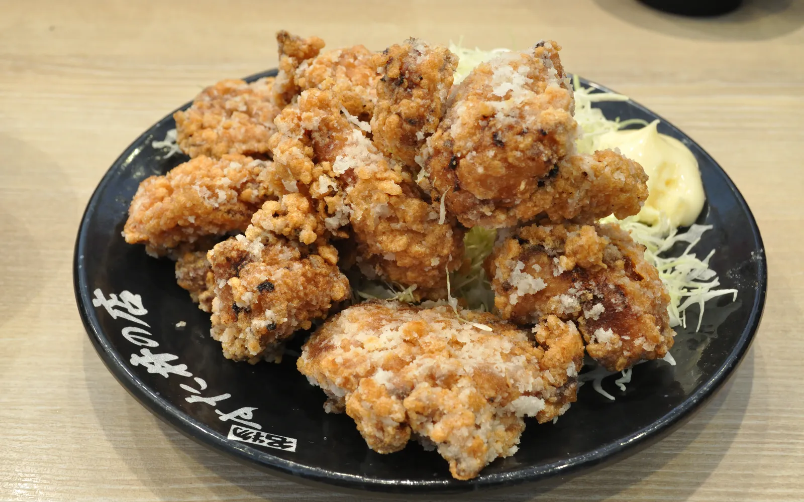 ปีกไก่ทอดสีทองกรอบโรยพริกไทยขาวบนจานกระดาษ ร้านสไตล์อิซากายะ