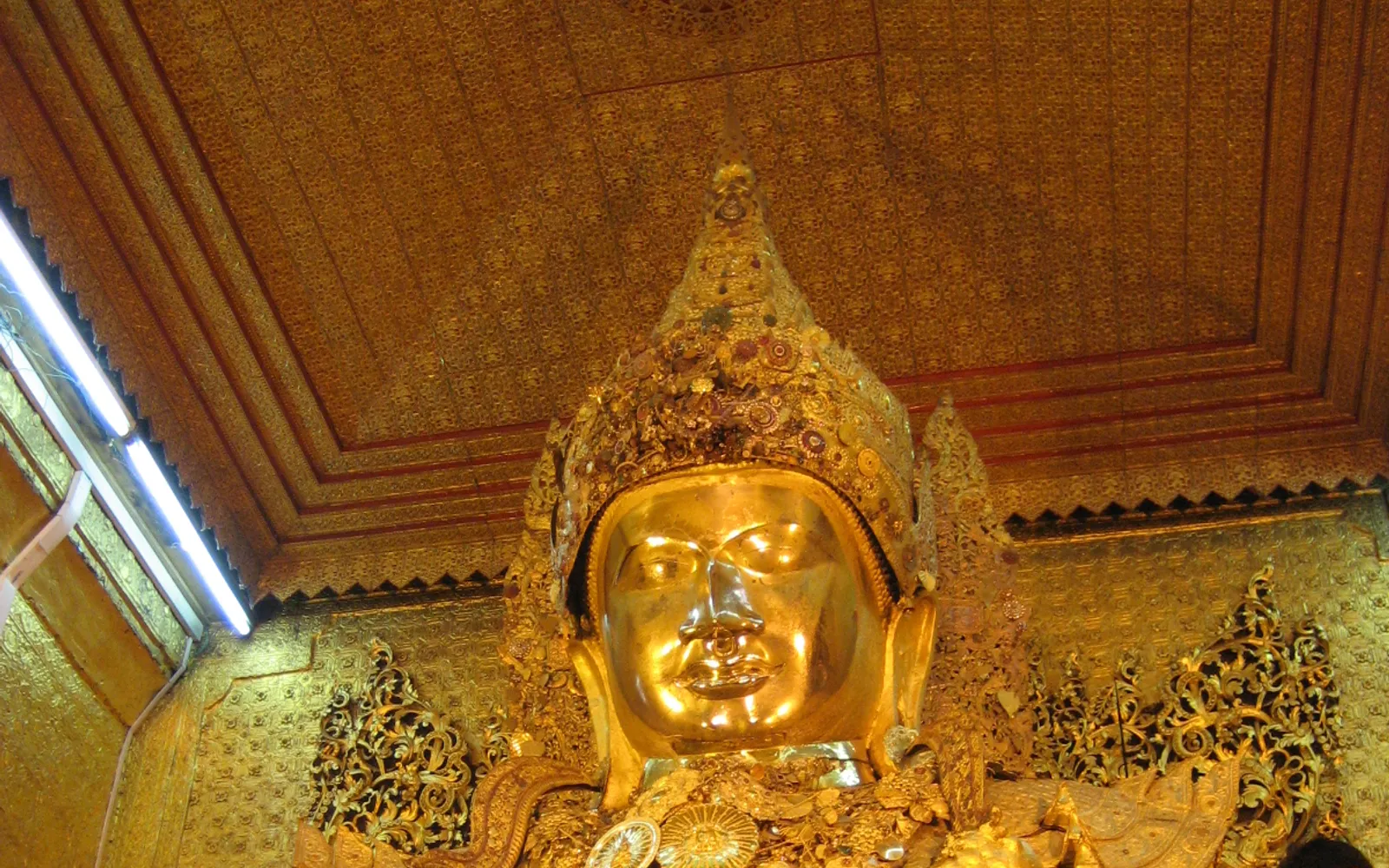 พระพุทธรูปมหามุนีองค์ใหญ่ปิดทองเหลืองอร่ามในวิหาร ผู้ศรัทธาเดินเข้าแถวถวายแผ่นทองคำเปลวล้อมรอบองค์พระ