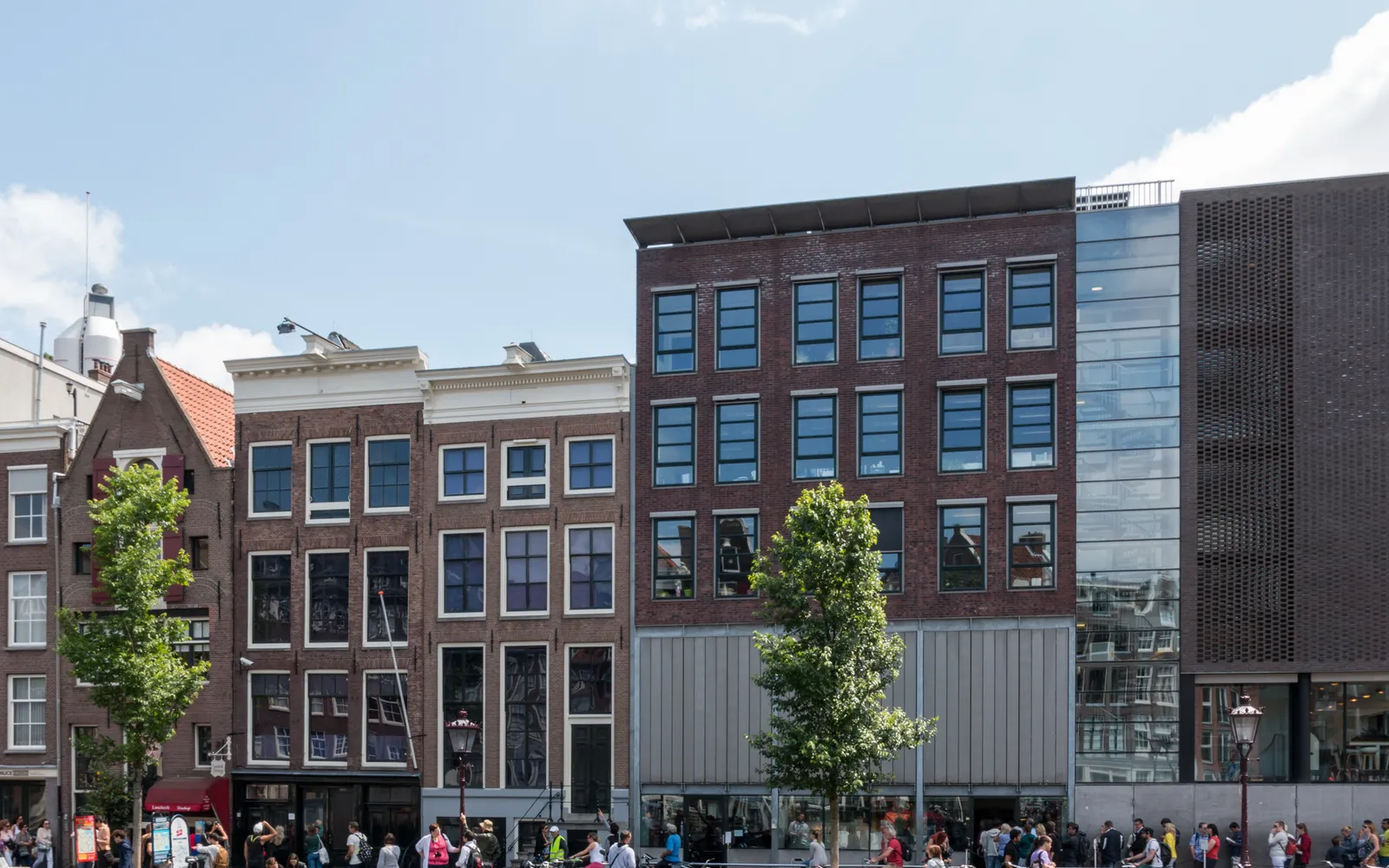 อาคารบ้านแถวสีเข้มริมคลอง Prinsengracht ประตูหน้าเล็กแคบ นักท่องเที่ยวต่อแถวยาวบนฟุตปาธ