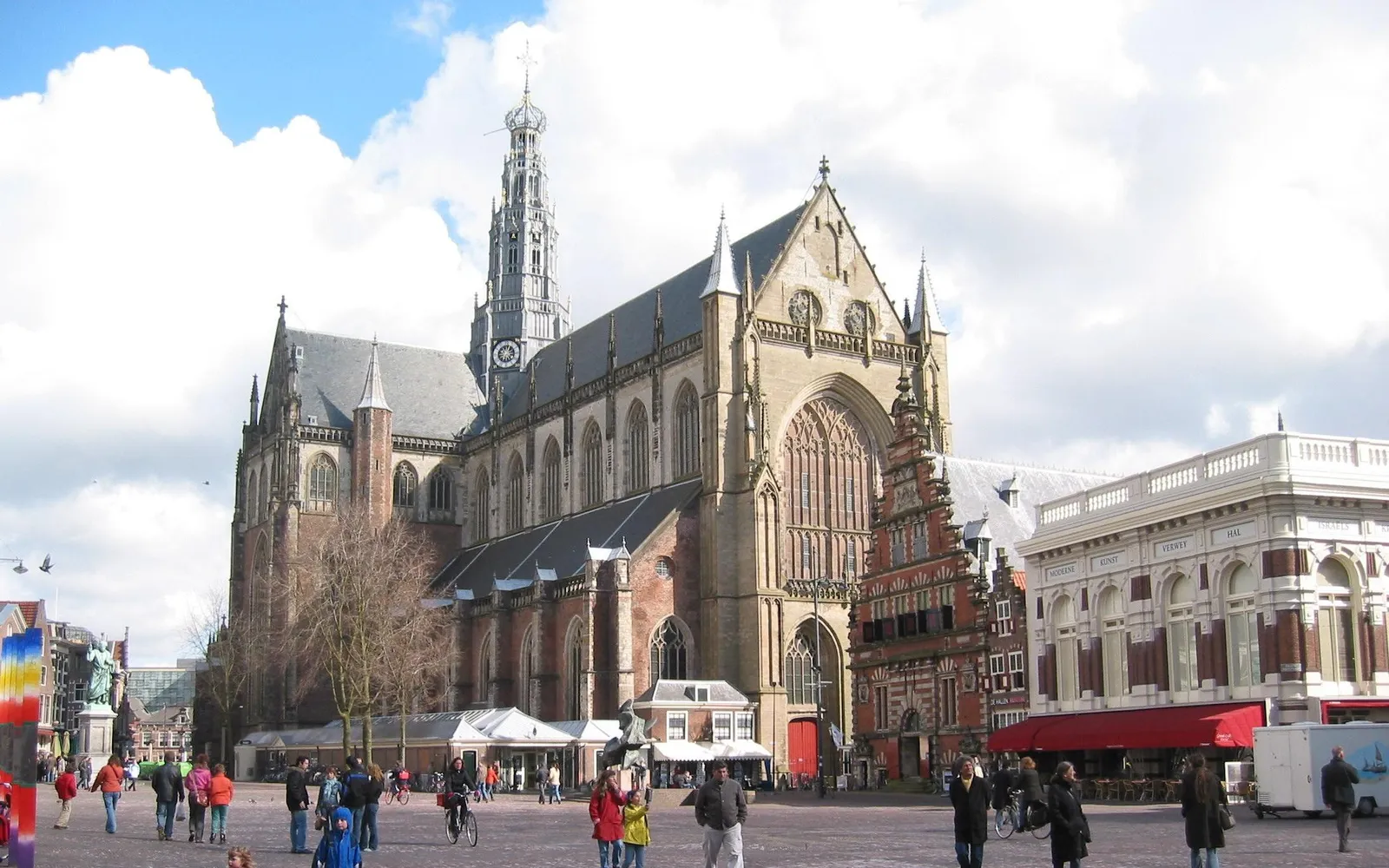 จัตุรัส Grote Markt ฮาร์เลม อาคาร Stadhuis สีขาวและโบสถ์ Grote Kerk ล้อมรอบลานกว้าง ร้านกาแฟระบายโต๊ะออกมาในแดดฤดูร้อน