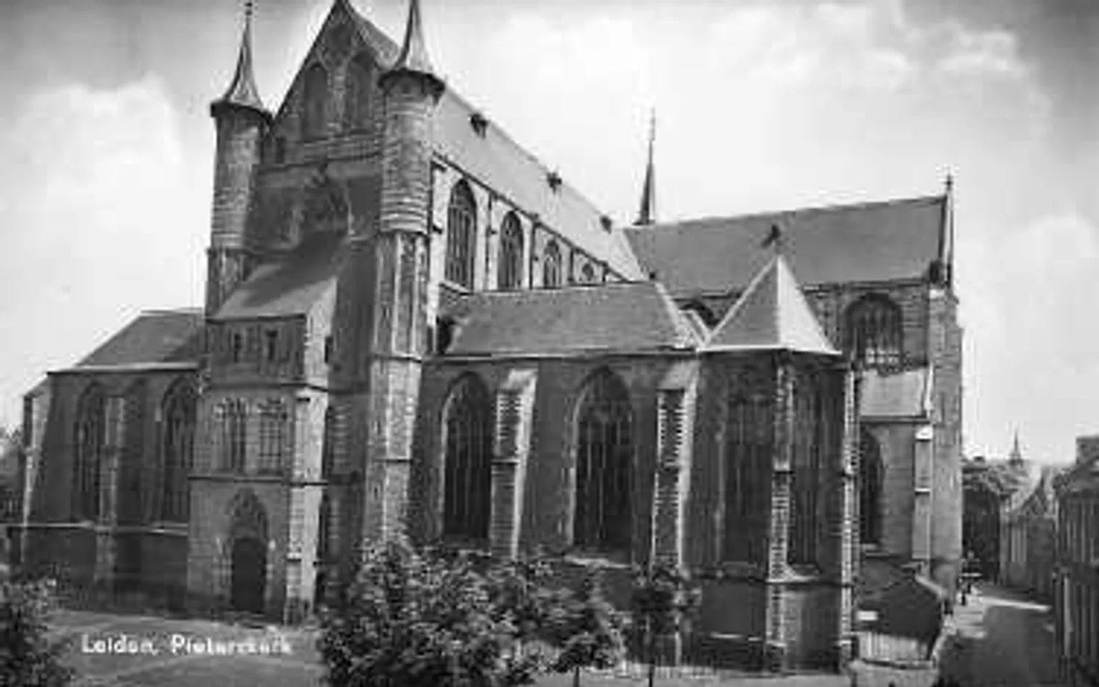 โบสถ์ Pieterskerk ไลเดน อาคารหินอิฐแดงสไตล์โกธิกโบราณทรงสูง ยอดหอคอยตัดกับท้องฟ้า ลานด้านหน้ามีต้นไม้ใหญ่ร่มครึ้ม