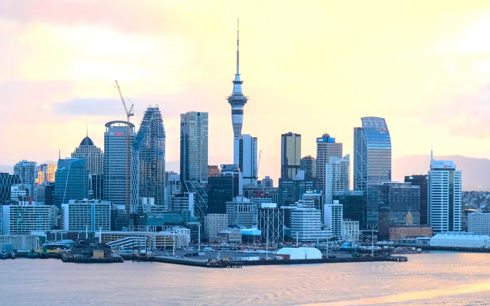 Viaduct Harbour โอ๊คแลนด์ยามเย็น เรือยอชต์ขาวจอดเรียงรายในอ่าวเล็ก ร้านอาหารและบาร์ริมน้ำสว่างไสว ผู้คนเดินเล่นบนทางเลียบชายฝั่ง