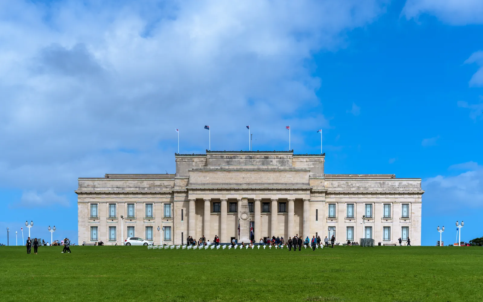 อาคารนีโอคลาสสิกสีขาวของ Auckland War Memorial Museum ตั้งบนเนินสูงใน Auckland Domain ล้อมรอบด้วยสนามหญ้าและต้นไม้เก่าแก่