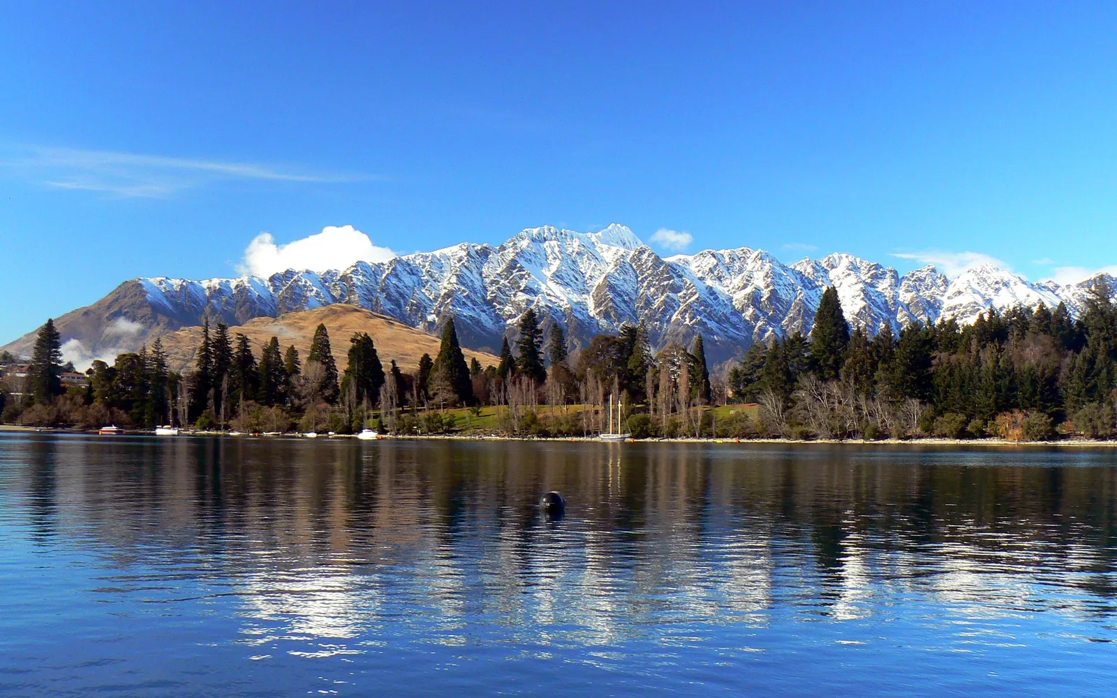 เทือกเขา The Remarkables ปกคลุมด้วยหิมะขาวสะอาด ลานสกีทอดยาวในแสงแดดยามเช้า ควีนส์ทาวน์และทะเลสาบวาคาทีปูมองเห็นได้เบื้องล่าง