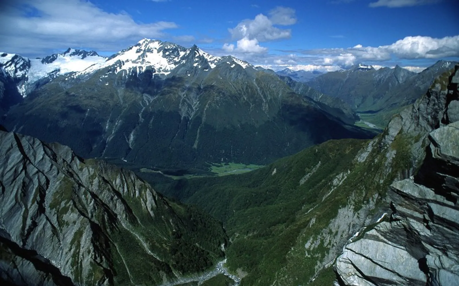 ยอดเขา Mount Aspiring ปลายแหลมปกคลุมด้วยหิมะเปล่งปลั่ง ล้อมรอบด้วยธารน้ำแข็งและหุบเขาสีเขียวใต้ท้องฟ้าสีฟ้า