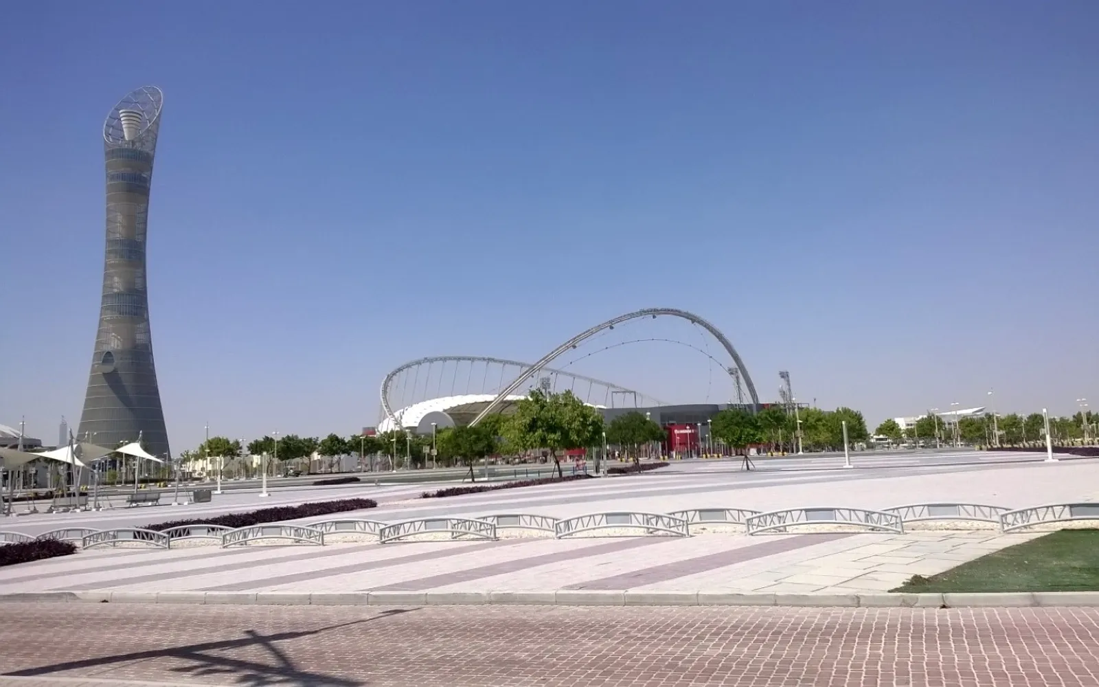 สนามหญ้าเขียวและทะเลสาบในสวนแอสไพร์ โดฮา พร้อมตึกทอร์ชเป็นฉากหลัง