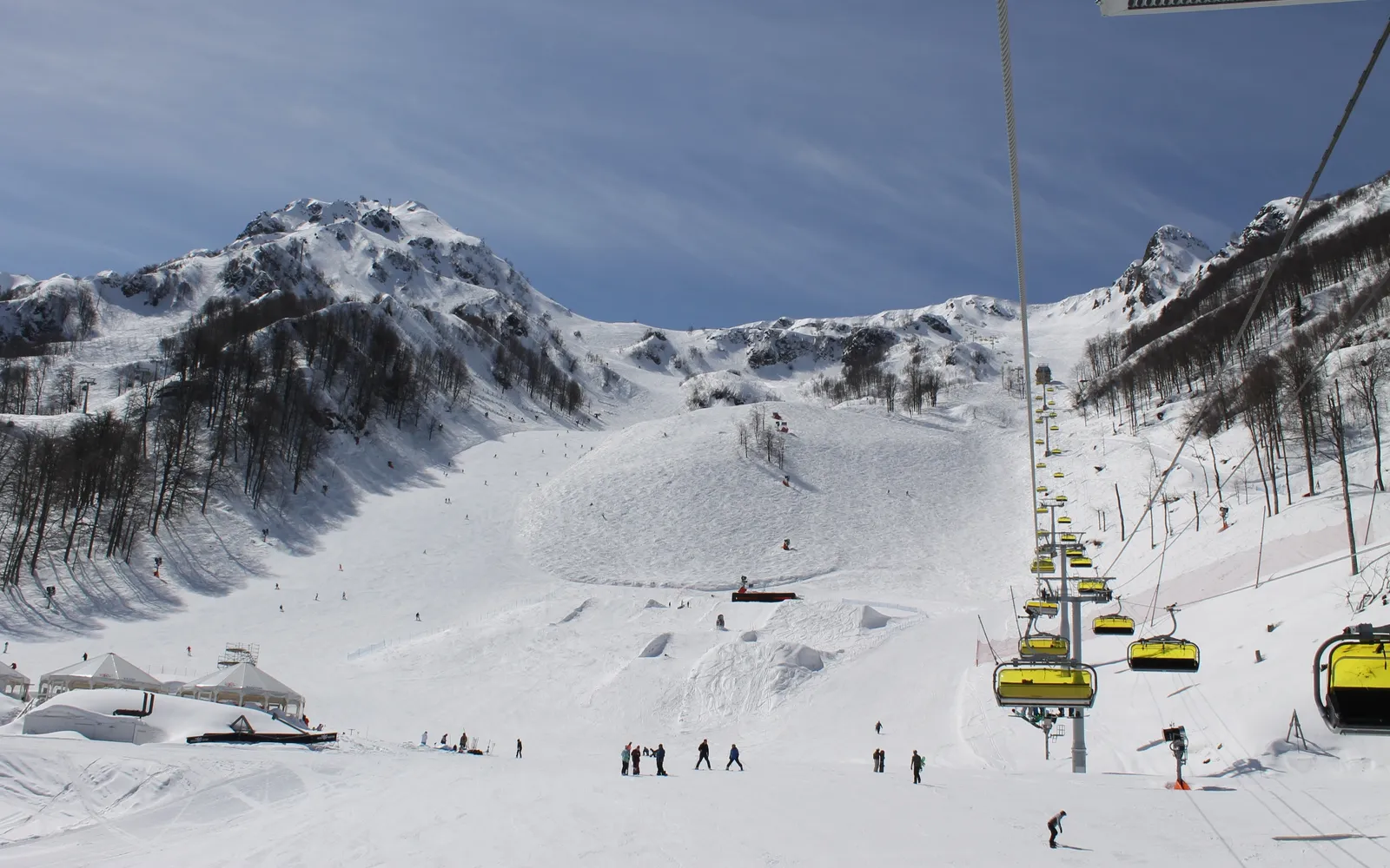 รีสอร์ท Rosa Khutor ท่ามกลางเทือกเขาคอเคซัส กระเช้าไฟฟ้าสีแดงลอยเหนือหุบเขา ยอดเขาหิมะขาวโพลนเป็นฉากหลัง