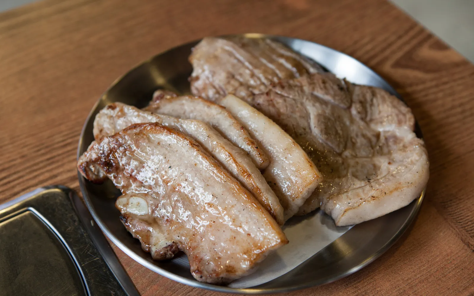 หมูสามชั้นย่างบนเตาถ่านในร้าน Korean BBQ พร้อมกิมจิและผักห่อหลากชนิดบนโต๊ะ