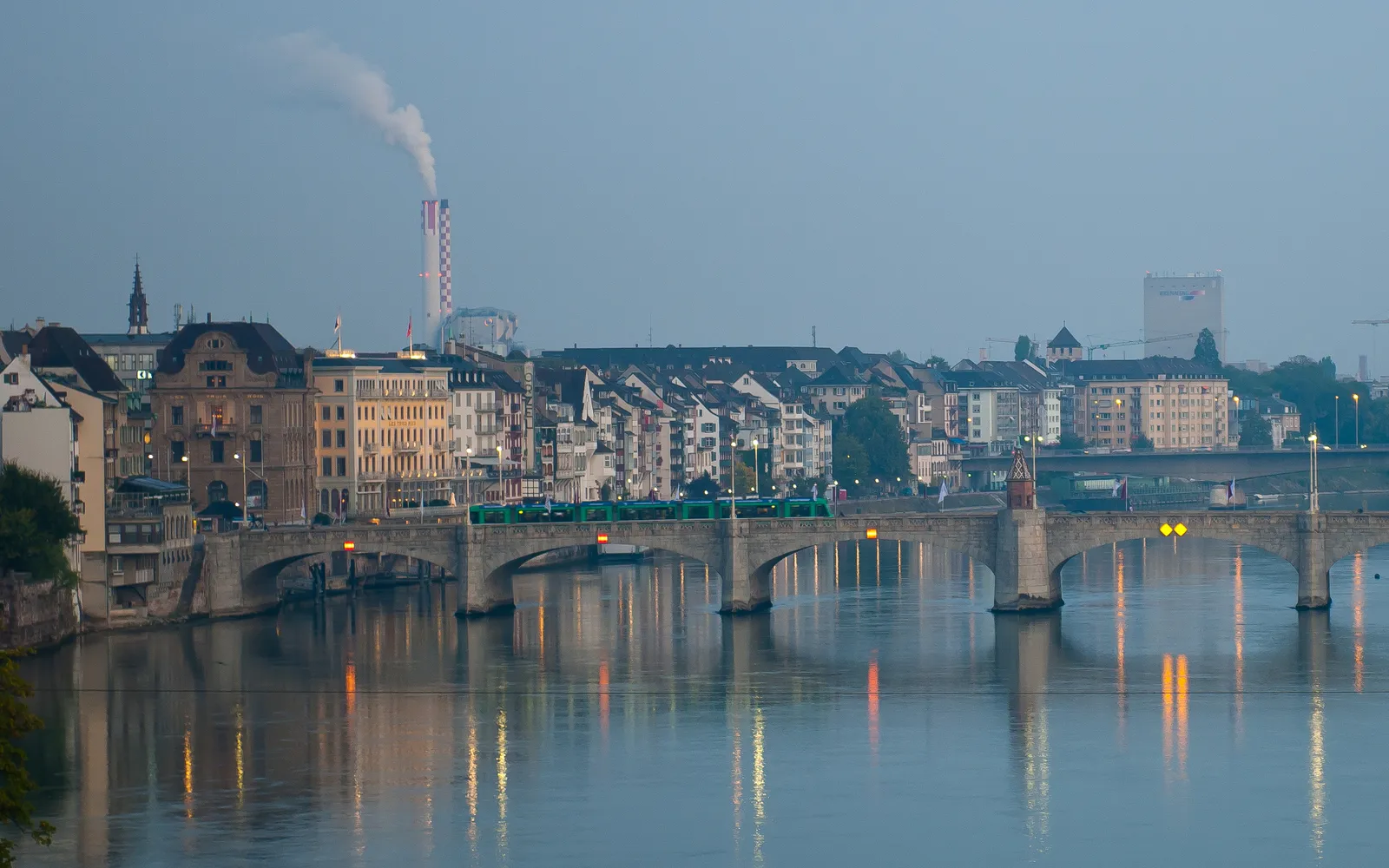 สะพาน Mittlere Brücke บาเซิลมองจากริมฝั่งน้ำ หอหินกลางสะพานสีเหลืองอ่อน มหาวิหาร Basel Minster ตั้งเด่นอยู่เบื้องหลัง