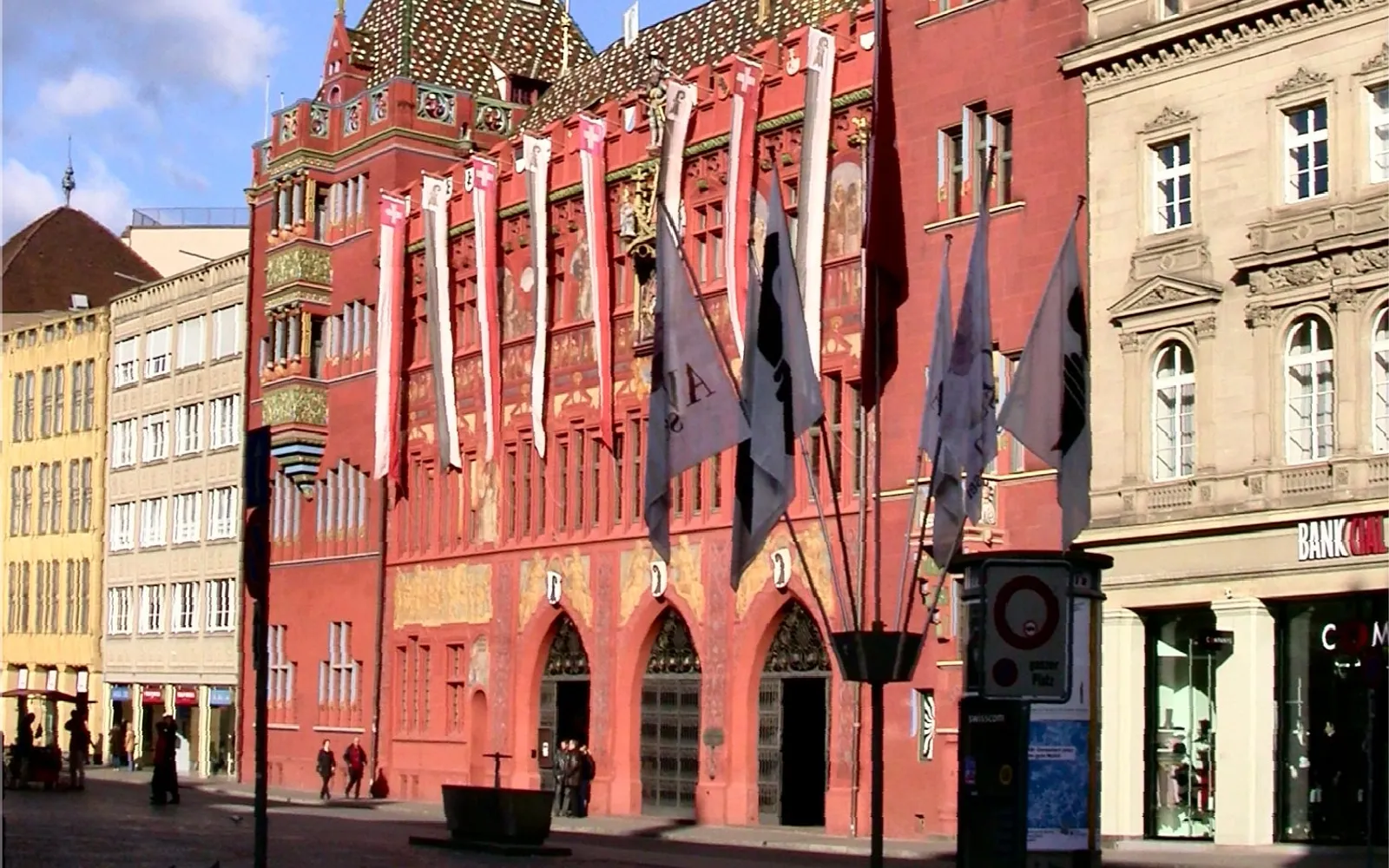 ศาลาว่าการบาเซิลสีแดงสดด้านหน้าจัตุรัส Marktplatz หอนาฬิกาสีทองตั้งตระหง่าน จิตรกรรมฝาผนังสีสันสดใสบนผนังด้านนอก