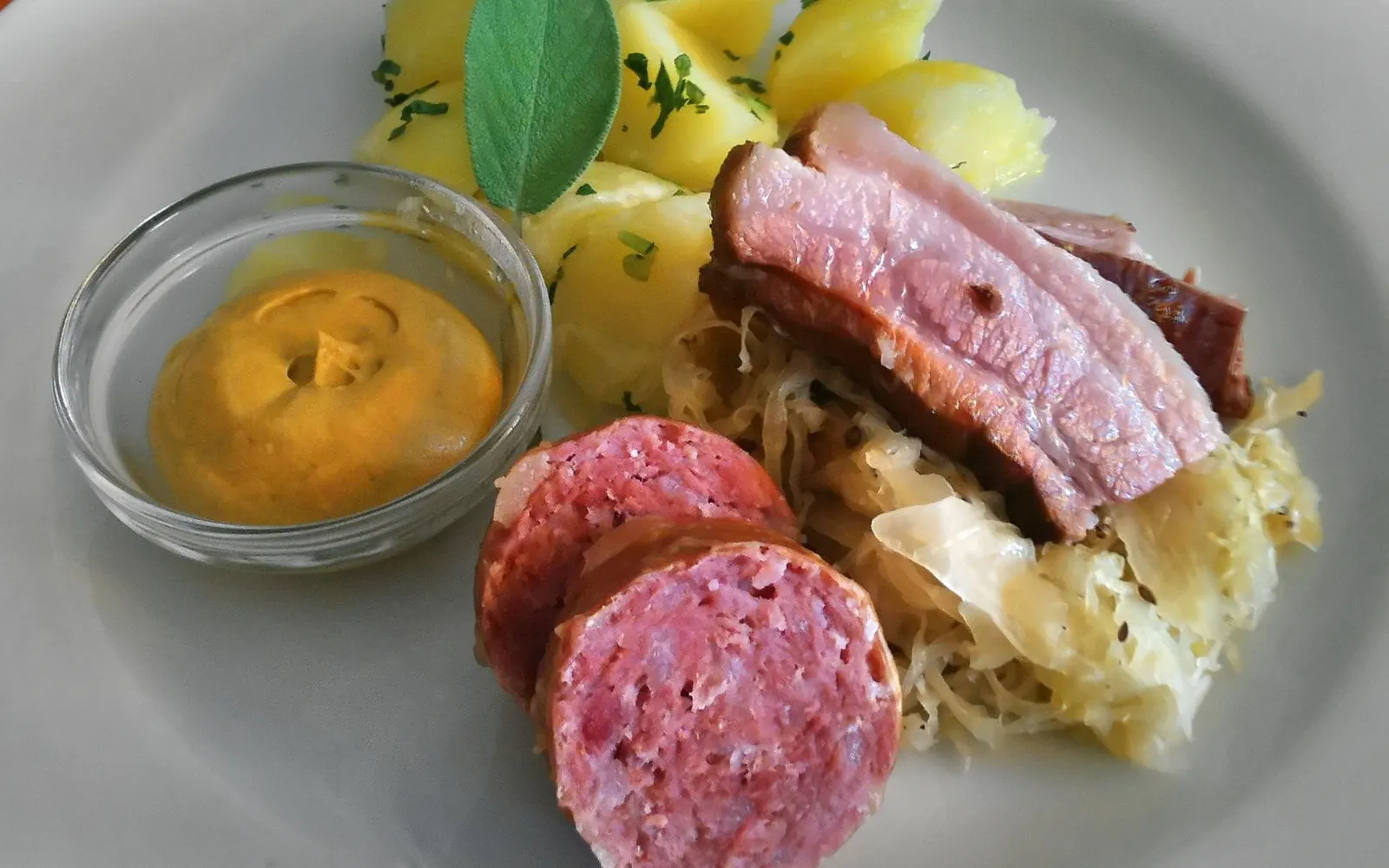 จาน Berner Platte ขนาดใหญ่บนโต๊ะไม้ มีหมูเค็ม ไส้กรอกหลายชนิด แฮมรมควัน กระดูกหมู กะหล่ำปลีดอง และถั่วเขียว เรียงอย่างสวยงาม