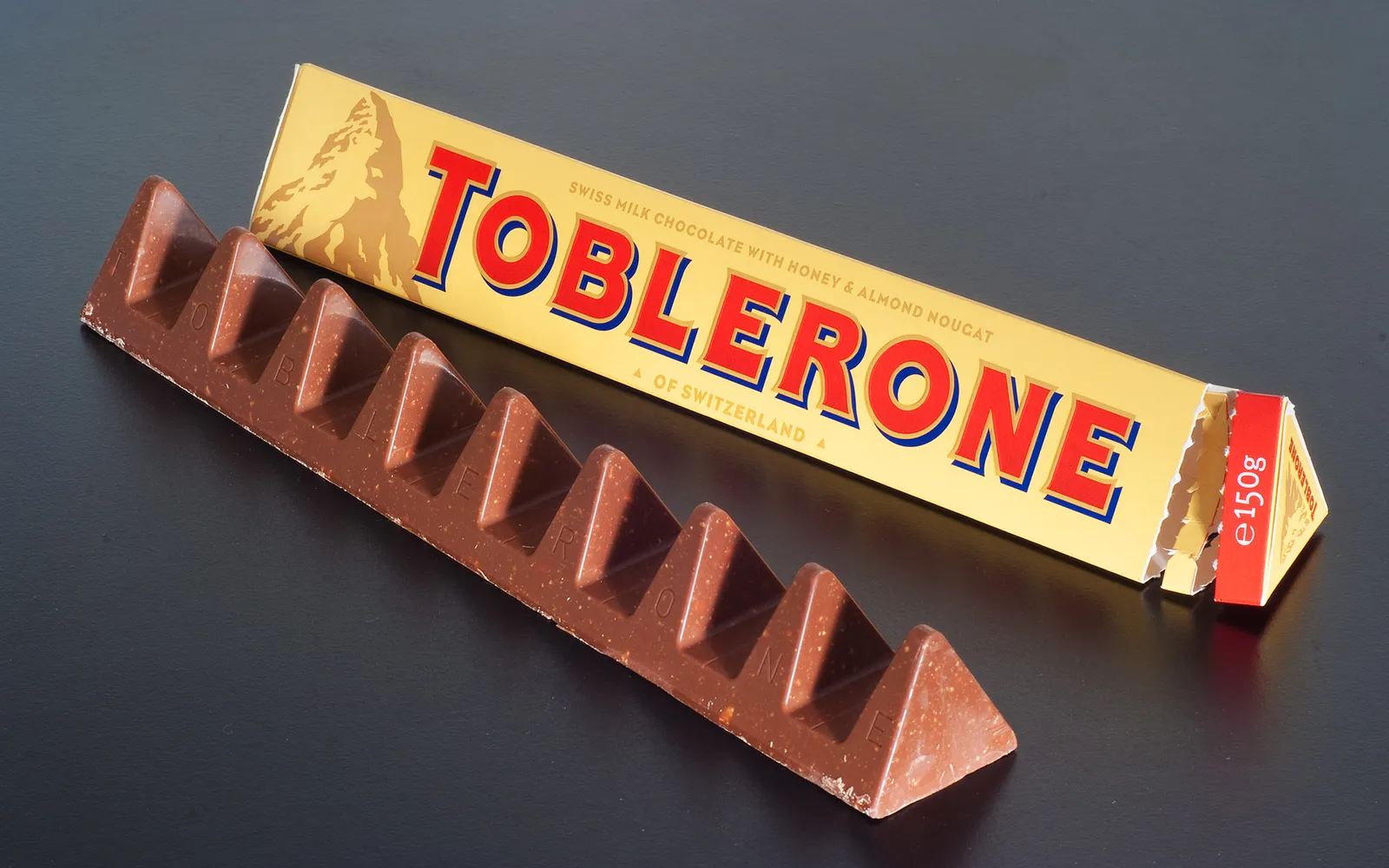 กล่องสามเหลี่ยมสีเหลืองทอง Toblerone วางบนชั้นวางในร้านของฝากเบิร์น โลโก้ภูเขา Matterhorn บนกล่องชัดเจน