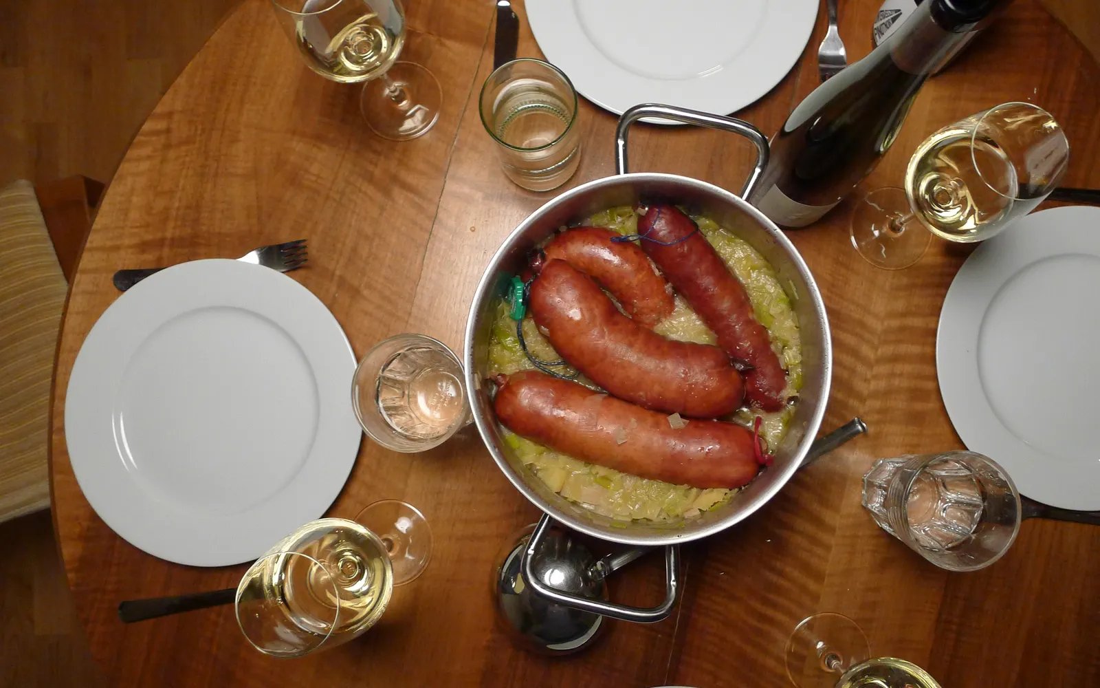 จาน Papet Vaudois ไส้กรอก Saucisson Vaudois สีแดงเนื้อนุ่มวางบนเตียงกะหล่ำปลีและต้นหอมตุ๋นน้ำเกรวี่สีเหลืองทอง