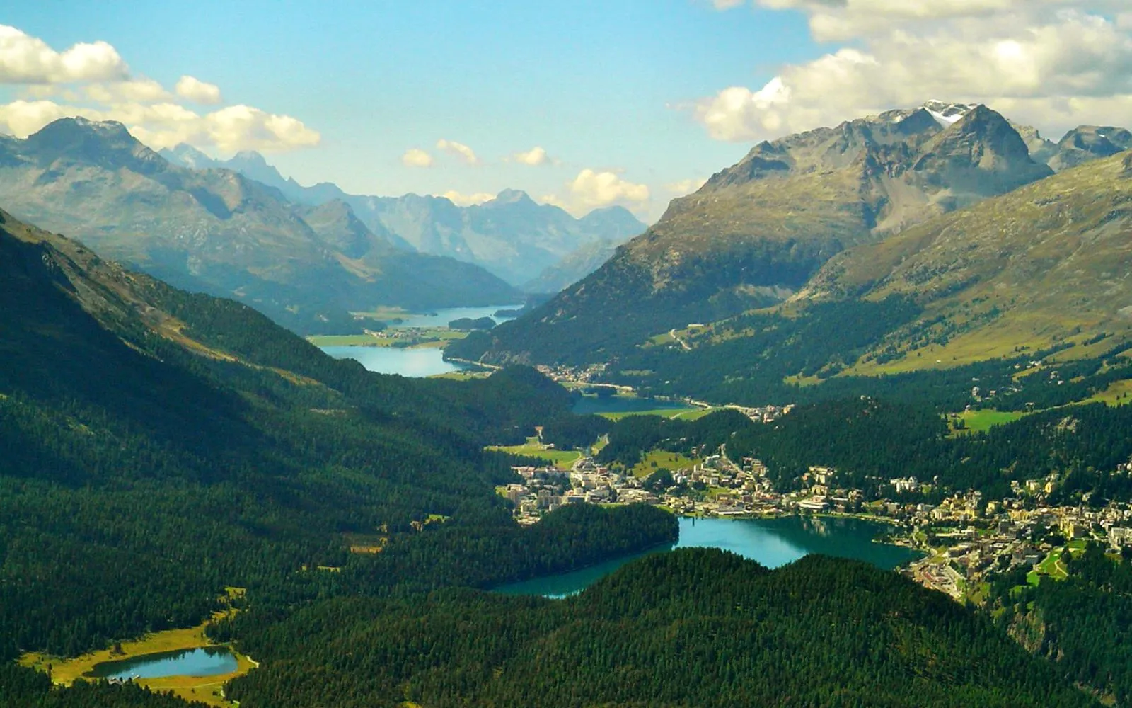 หุบเขา Engadin ในฤดูใบไม้ร่วง ทุ่งหญ้าเปลี่ยนเป็นสีทองและส้ม ทะเลสาบเรียงราย 5 แห่งสะท้อนเทือกเขา Bernina พื้นหลังสีน้ำเงิน