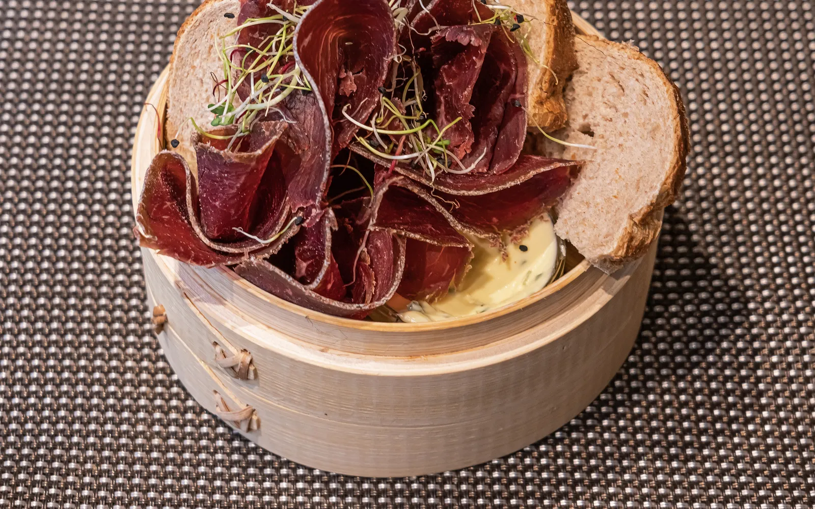 Bündnerfleisch เนื้อวัวตากลมสีแดงเข้มหั่นแผ่นบางเฉียบเรียงบนจานชาม ริมเป็นขนมปัง Rye สีเข้มและเนยอัลไพน์
