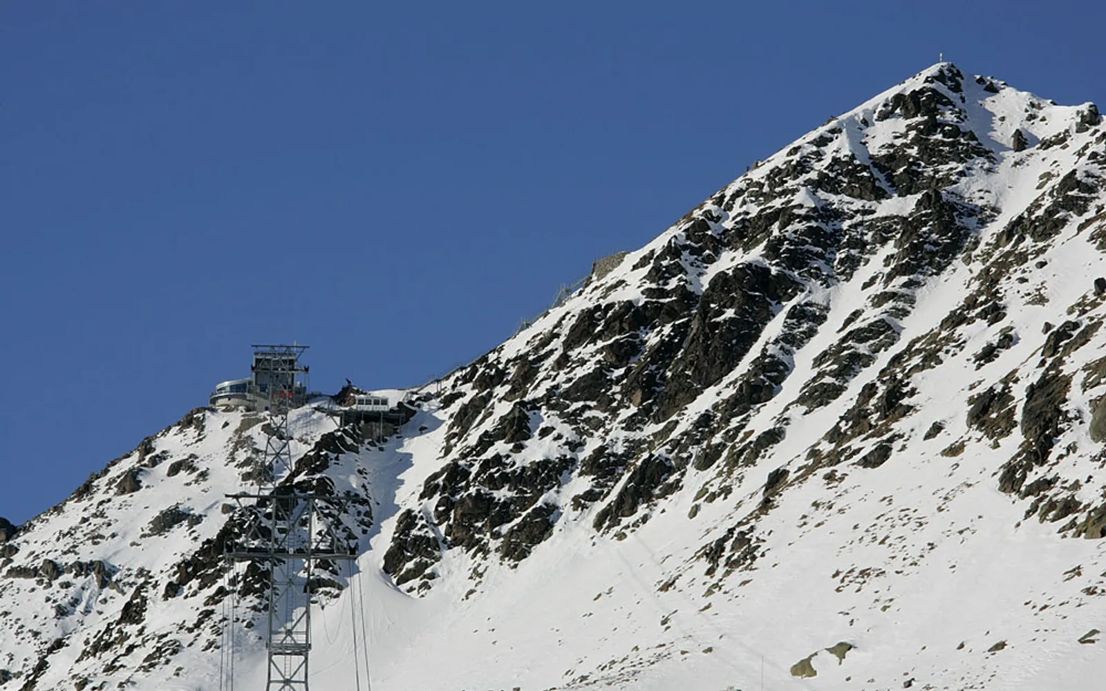 ยอดเขา Piz Nair สูง 3,057 เมตร มองเห็นหุบเขา Engadin ทะเลสาบสีเทอร์คอยซ์เรียงราย และเทือกเขาแอลป์ยาวสุดขอบฟ้า ใต้ท้องฟ้าสีน้ำเงินเข้มระดับสูง