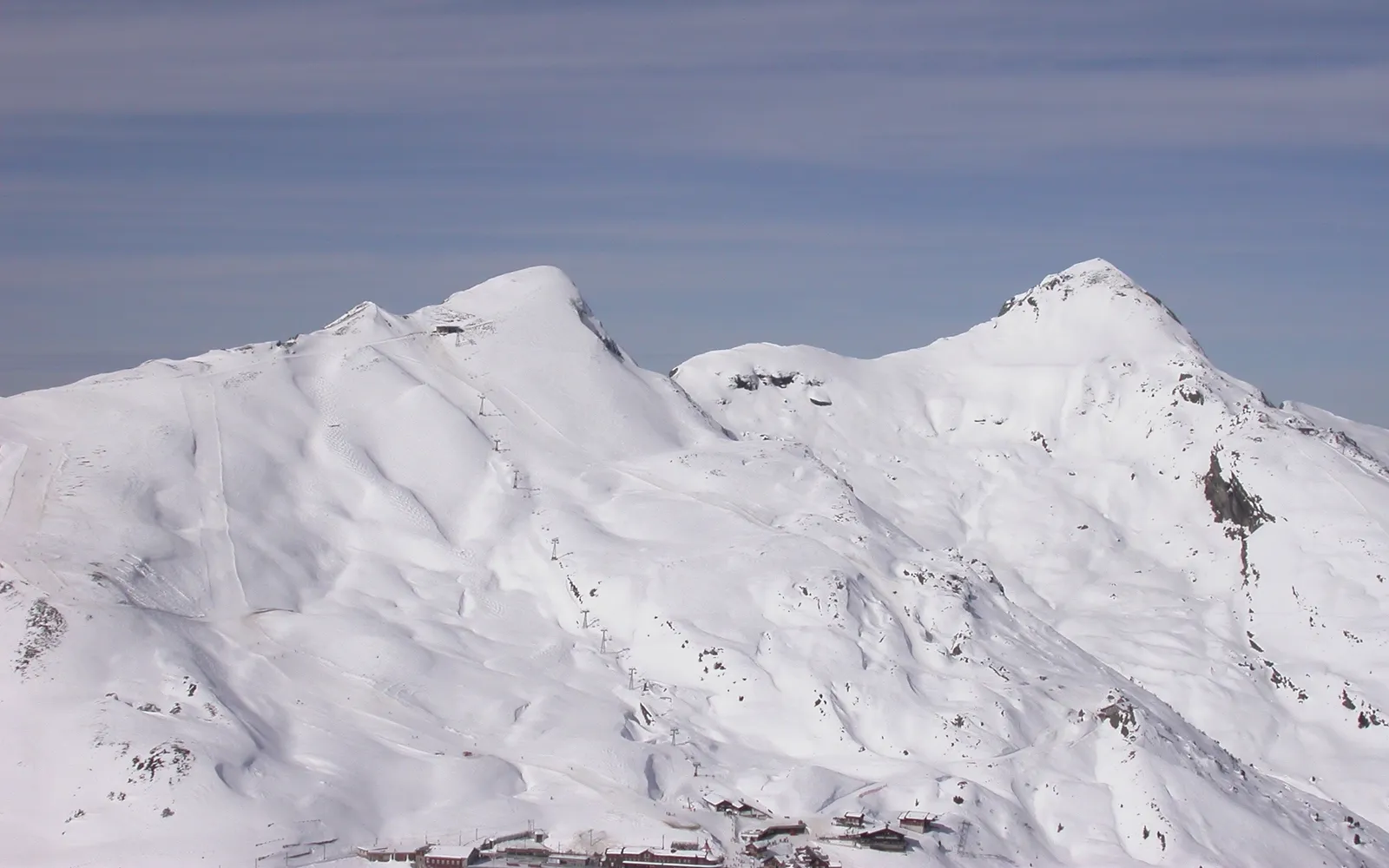ลาดสกี Lauberhorn เวงเงน หิมะขาวสะอาดลาดลงมาตามสันเขา ธงสีส้มและน้ำเงินปักบอกเส้นทางแข่ง สกีเออร์สองสามคนเฉือนหิมะลงมา